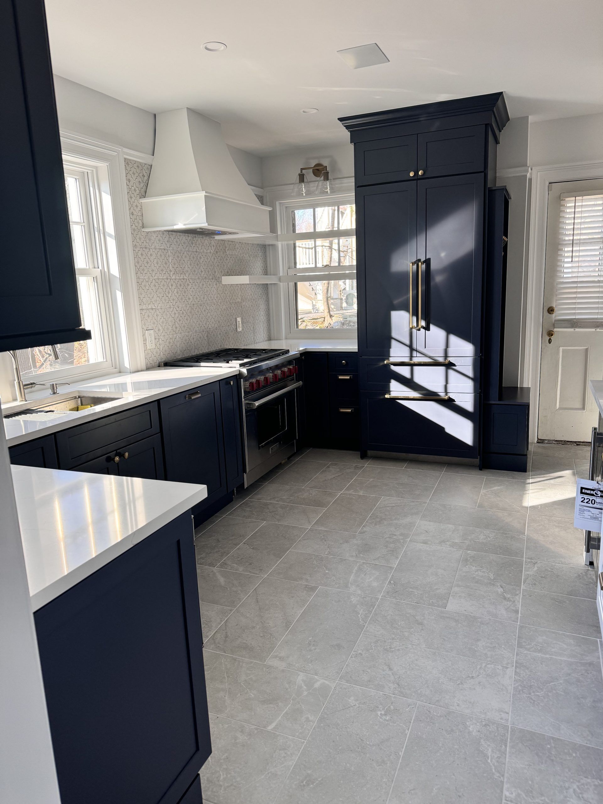 Modern kitchen with navy cabinets, white countertops, and large windows with sunlight.