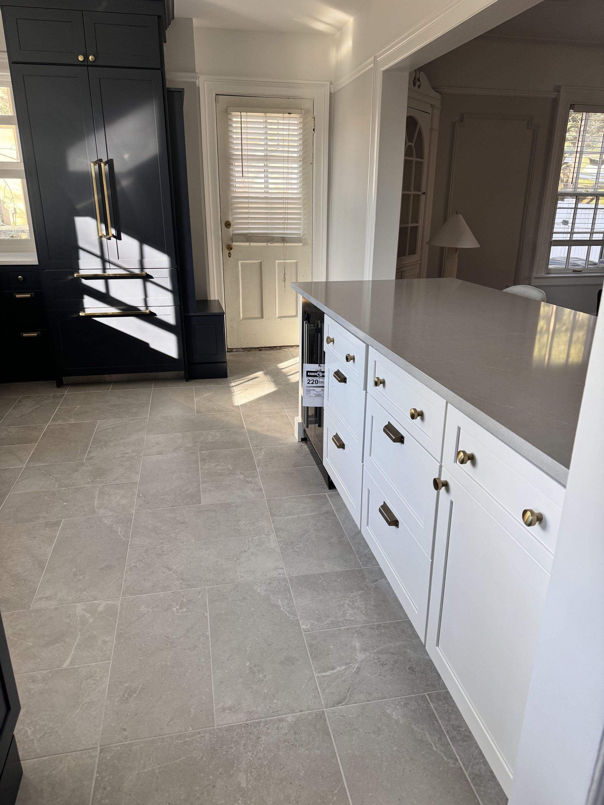 Modern kitchen with white cabinets, gray tile floor, and a dark black refrigerator by the doorway