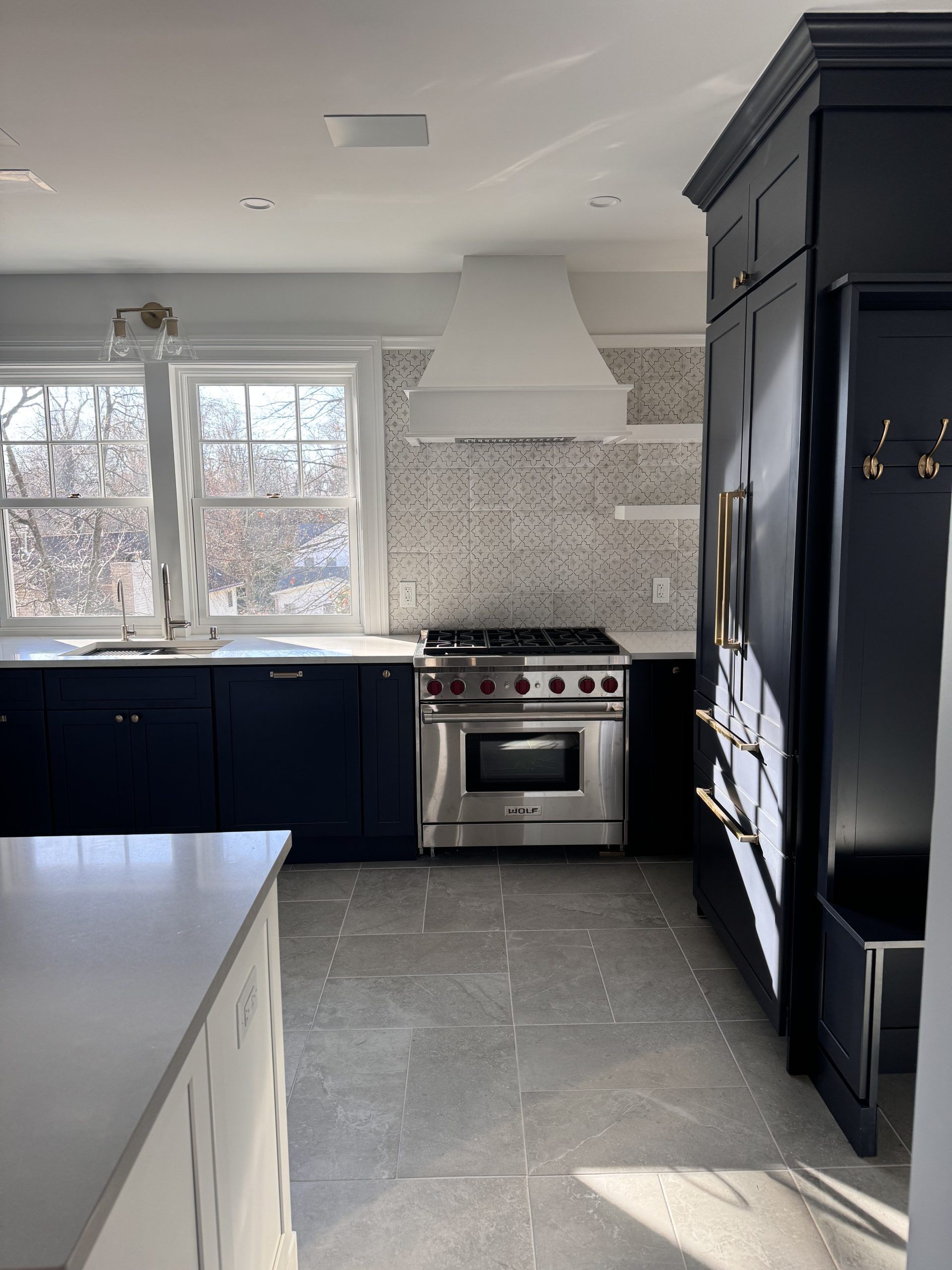 Modern kitchen with dark cabinets, stainless steel stove, white hood, tiled backsplash, and bright windows