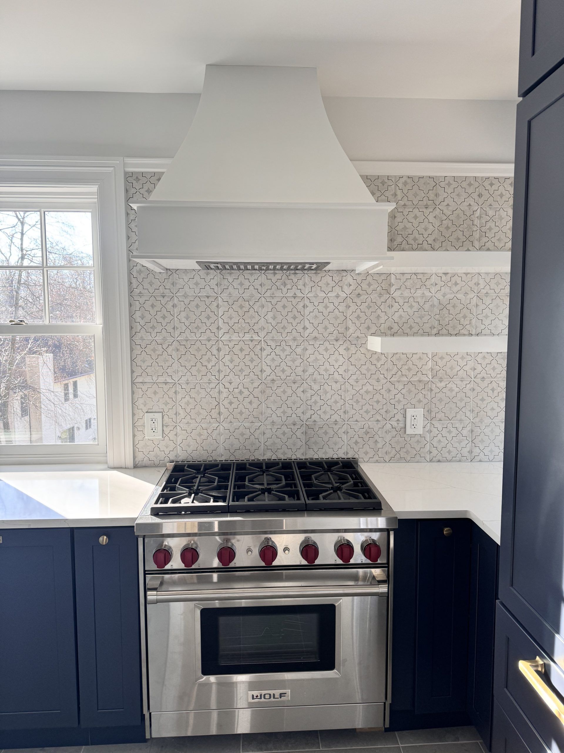 Modern kitchen with stainless steel stove, white range hood, blue cabinets, and patterned backsplash