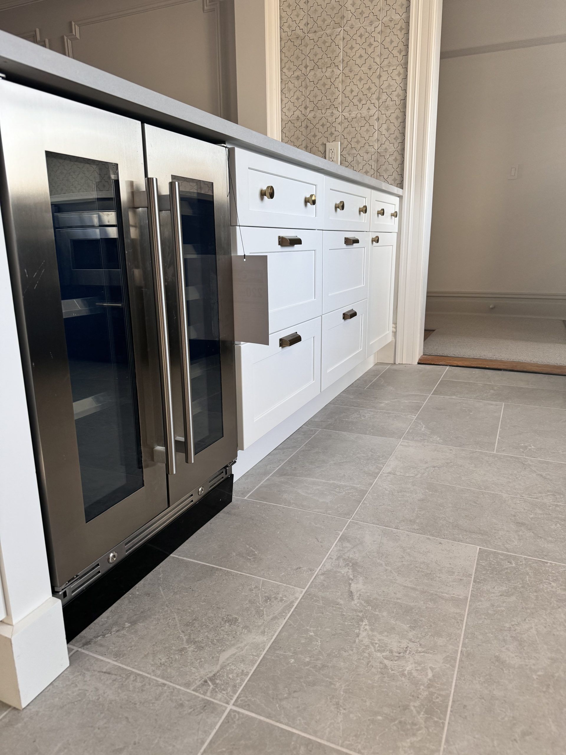 Modern kitchen with stainless steel oven, white cabinets, and gray tile flooring
