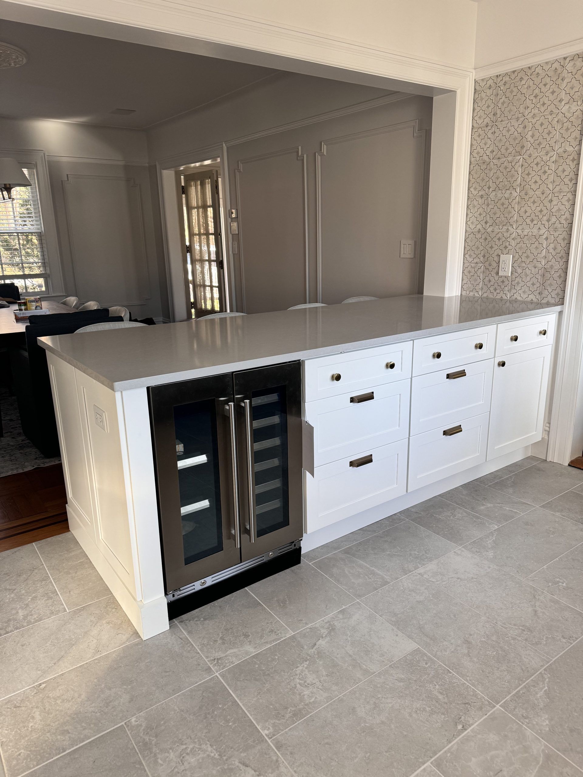 Kitchen peninsula with white cabinets, black countertop, and built-in beverage fridge in a tiled room