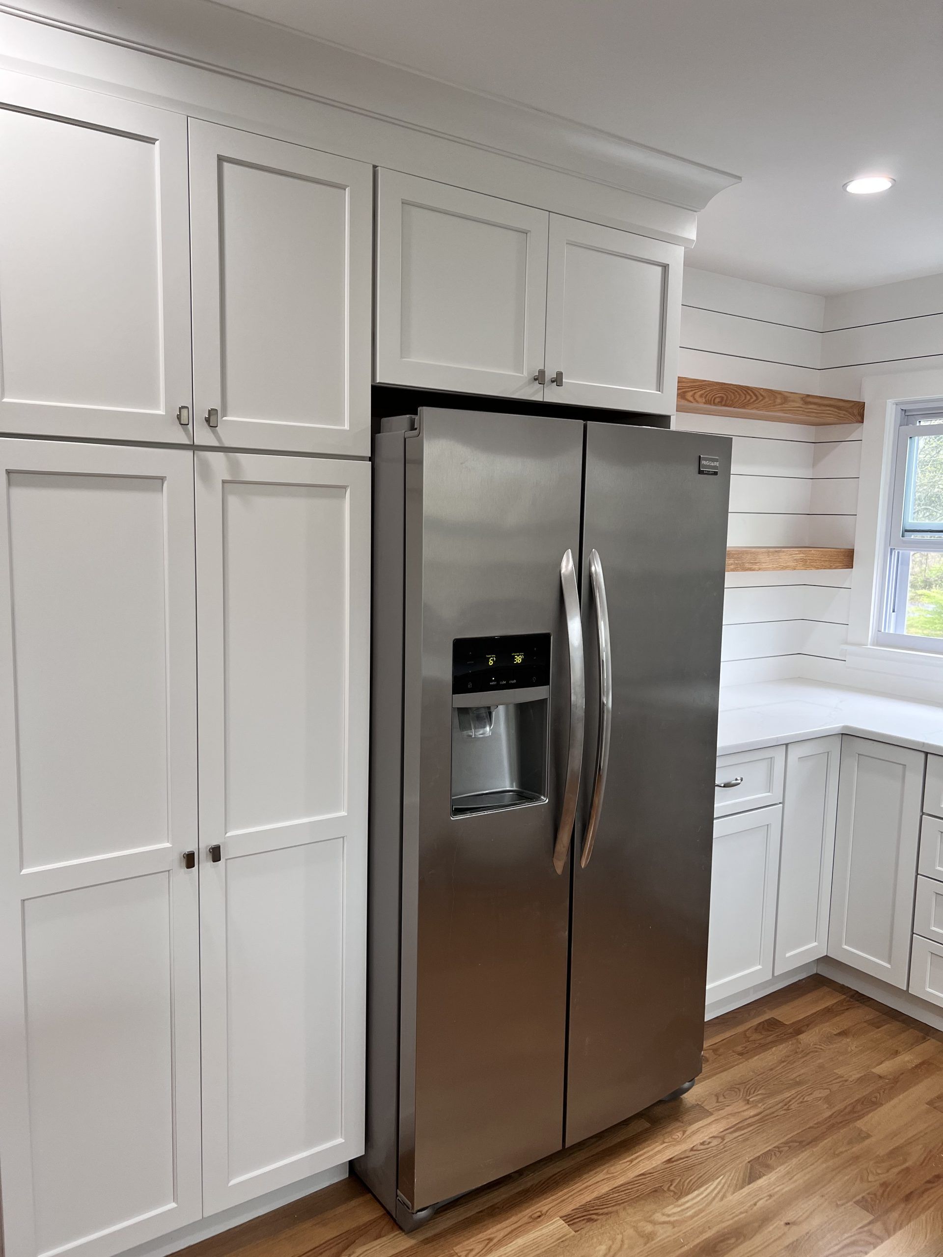Bright white kitchen with stainless steel refrigerator and wood flooring