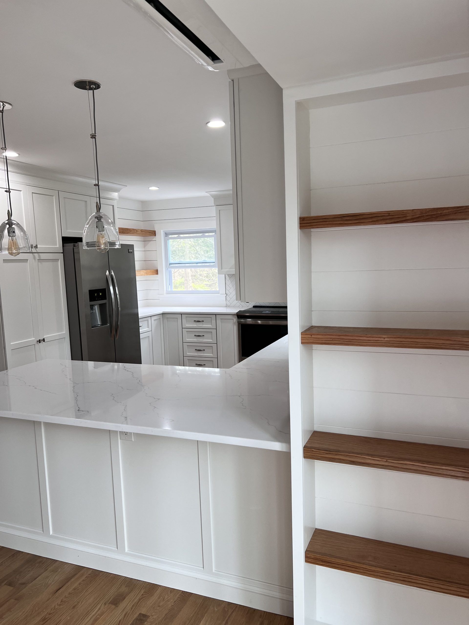Open kitchen pass-through with white counters, stainless fridge, and built-in wooden shelves.