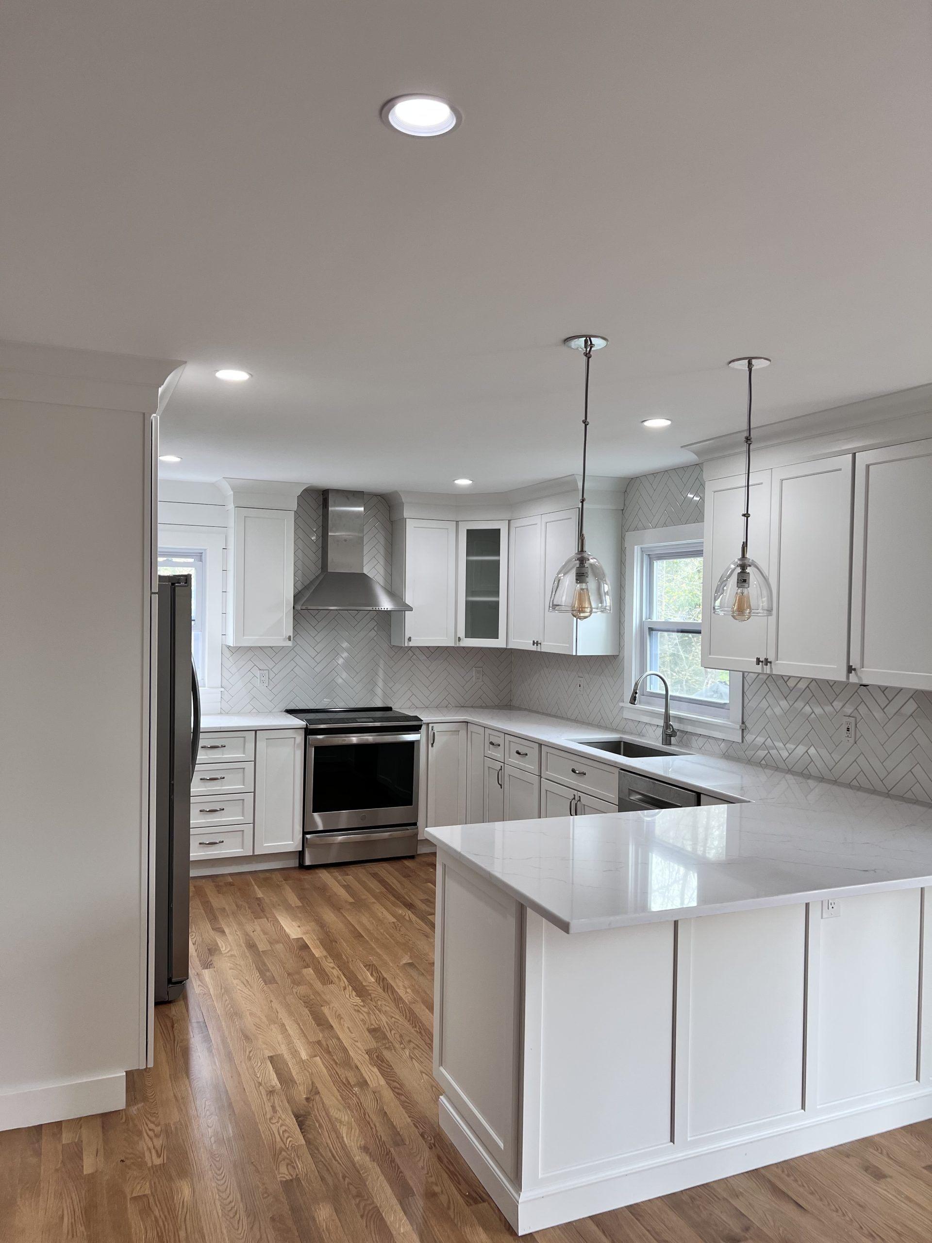Bright modern kitchen with white cabinets, island, stainless stove, and wood floors
