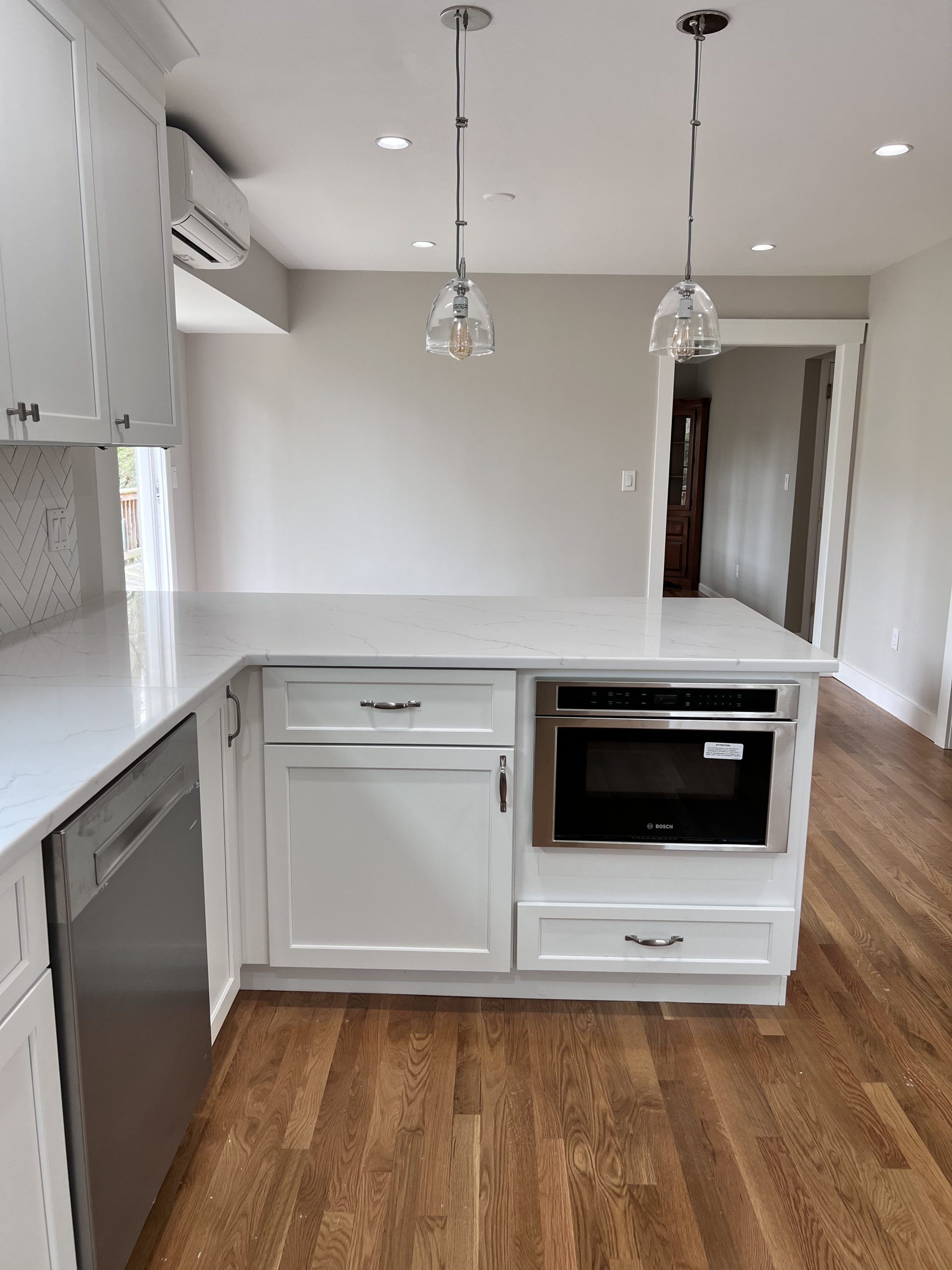 Modern kitchen with white cabinets, island, pendant lights, and wood flooring