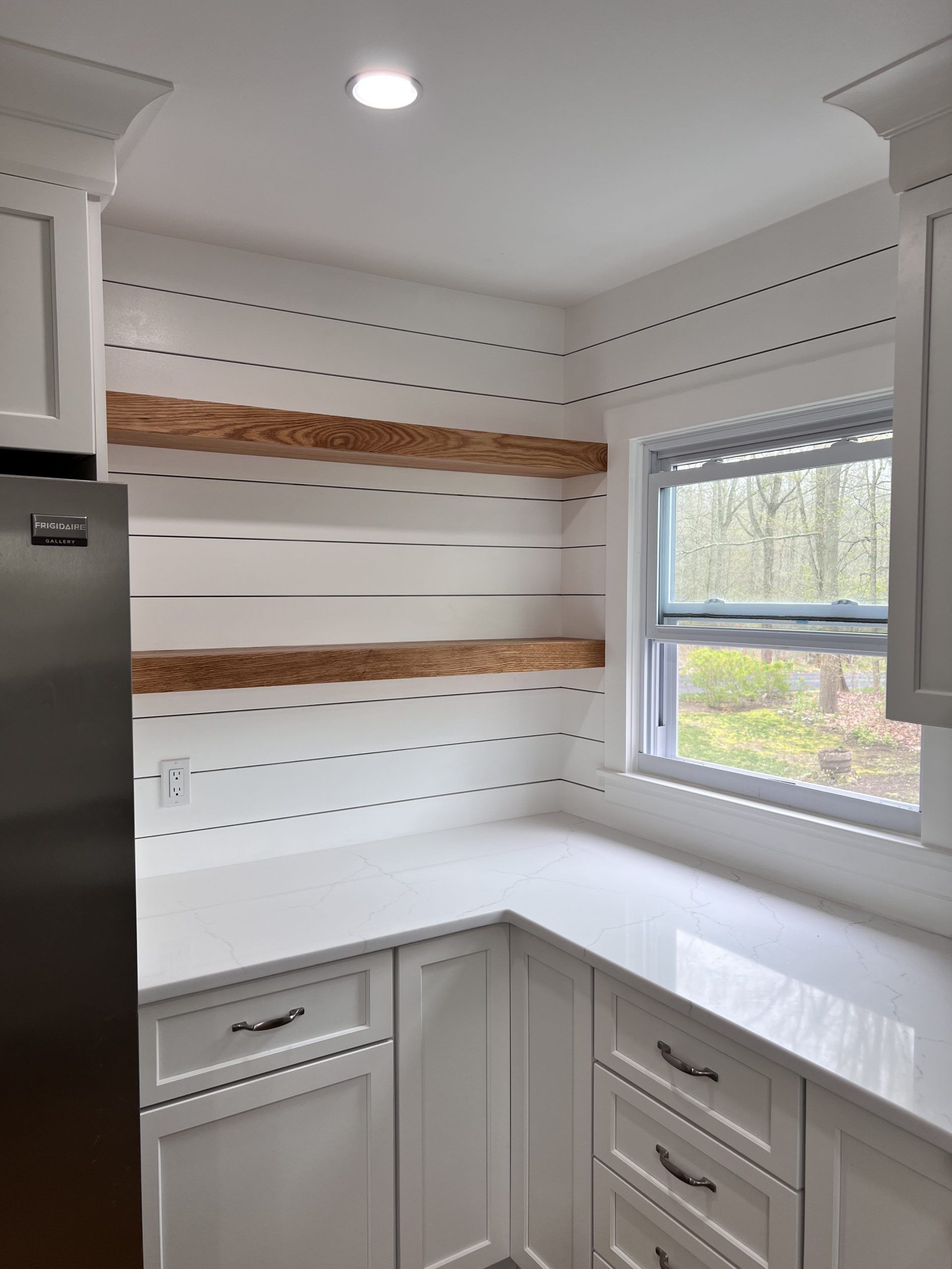 White kitchen corner with open shelving and a window above a light countertop