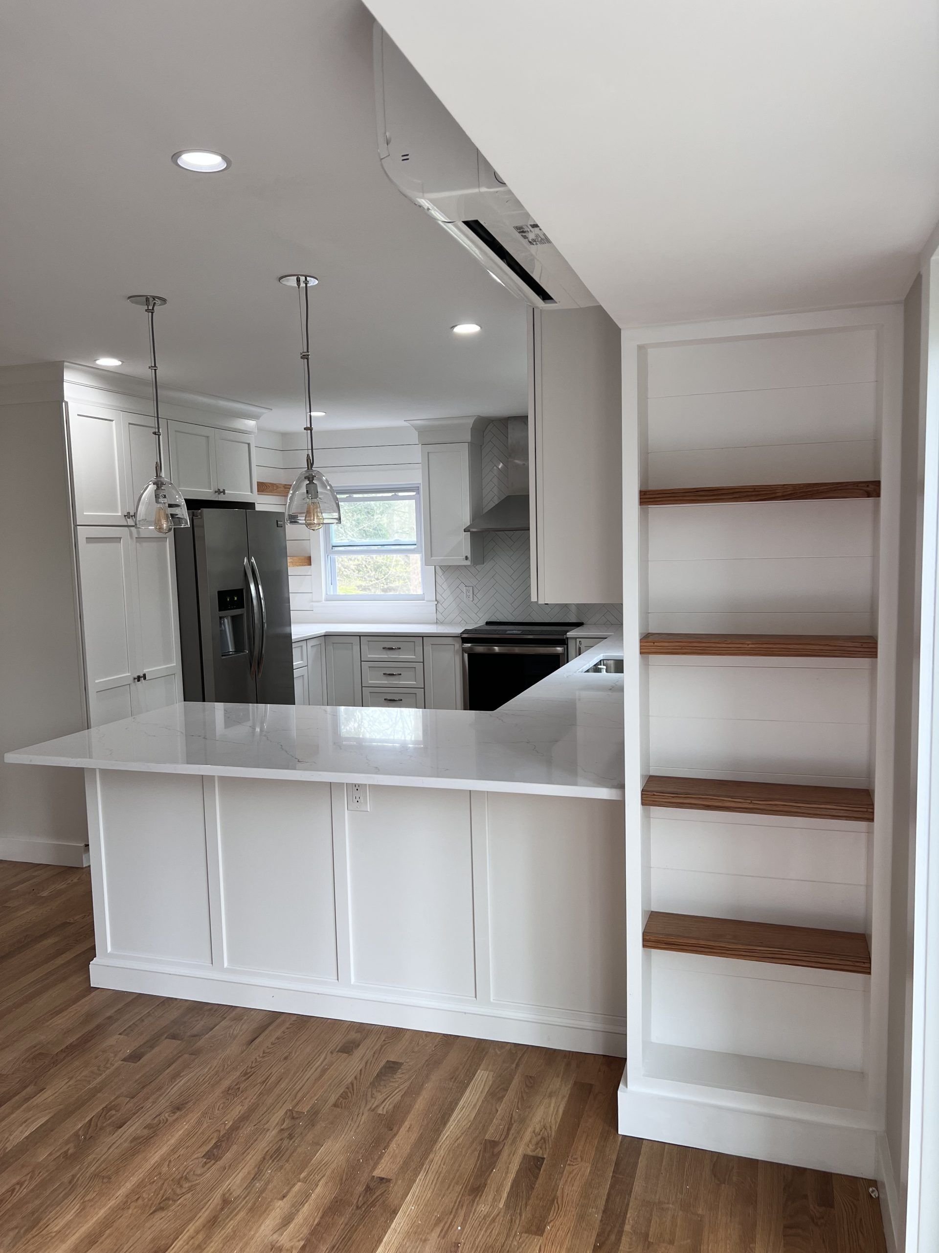 Bright kitchen with white cabinets, wood floors, and a narrow staircase with open wooden steps.