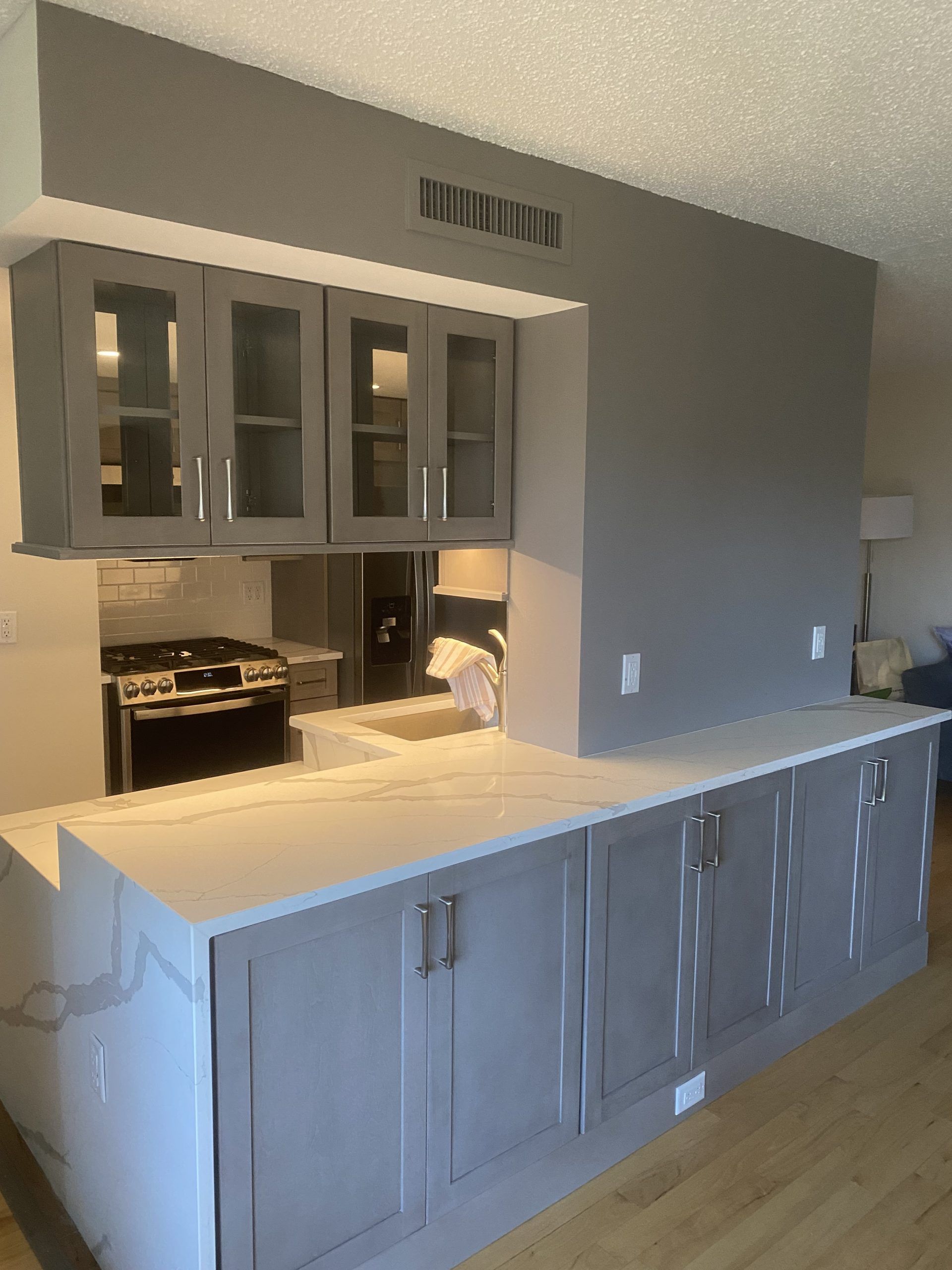 Gray kitchen with white countertop, upper glass cabinets, and built-in beverage cooler against a gray wall