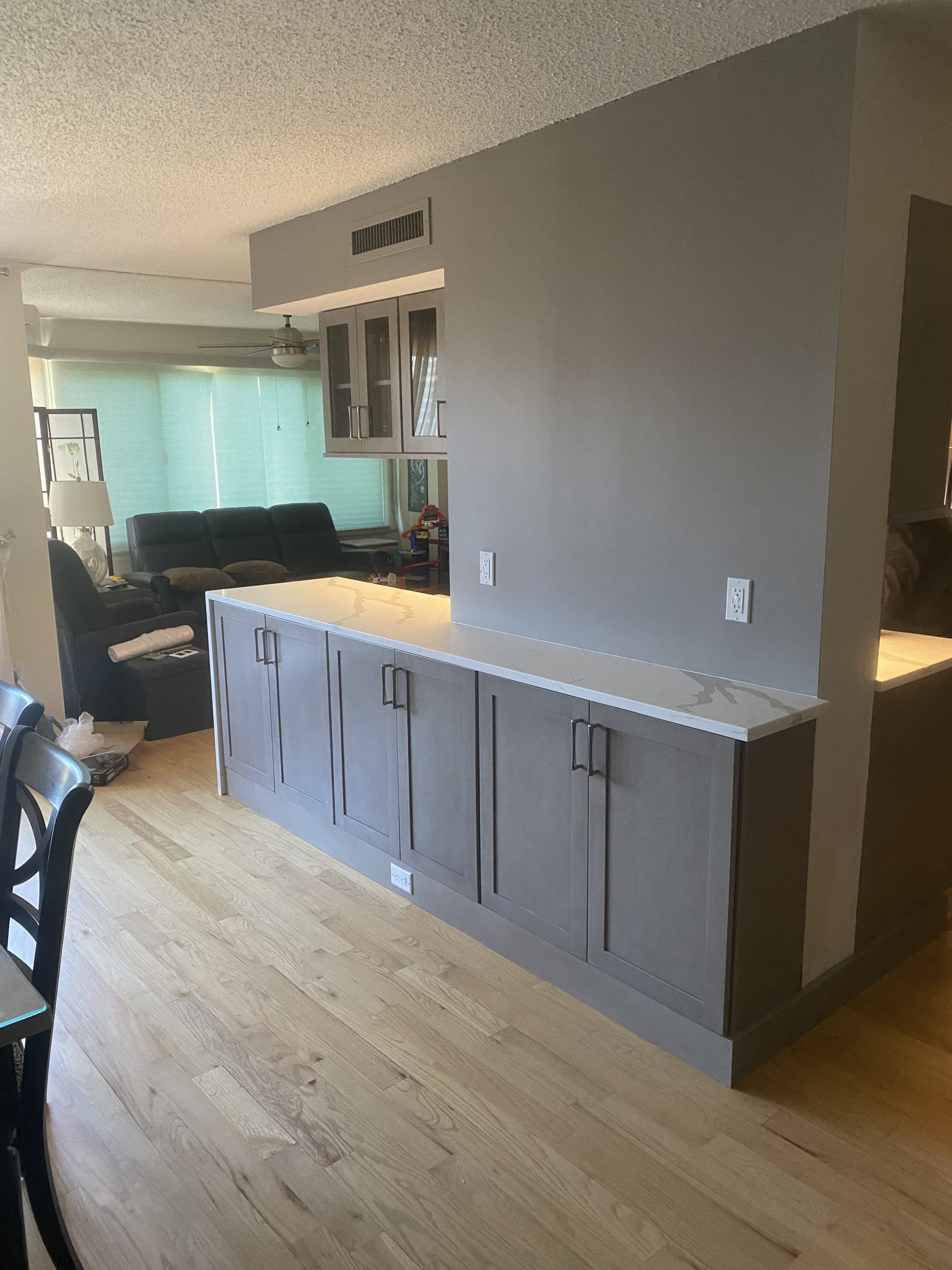 Modern kitchen with gray cabinets and a light wood floor opening to a living room.