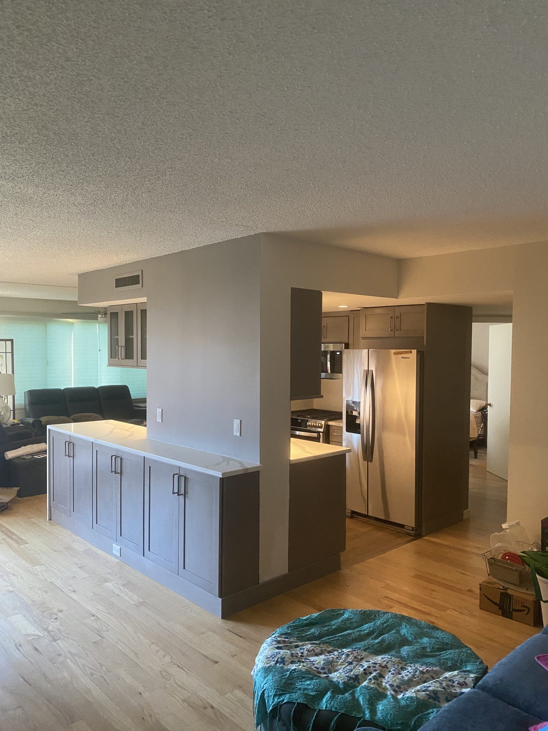 Open-concept kitchen and living room with gray cabinets, stainless fridge, wood floors, and blue sofa.