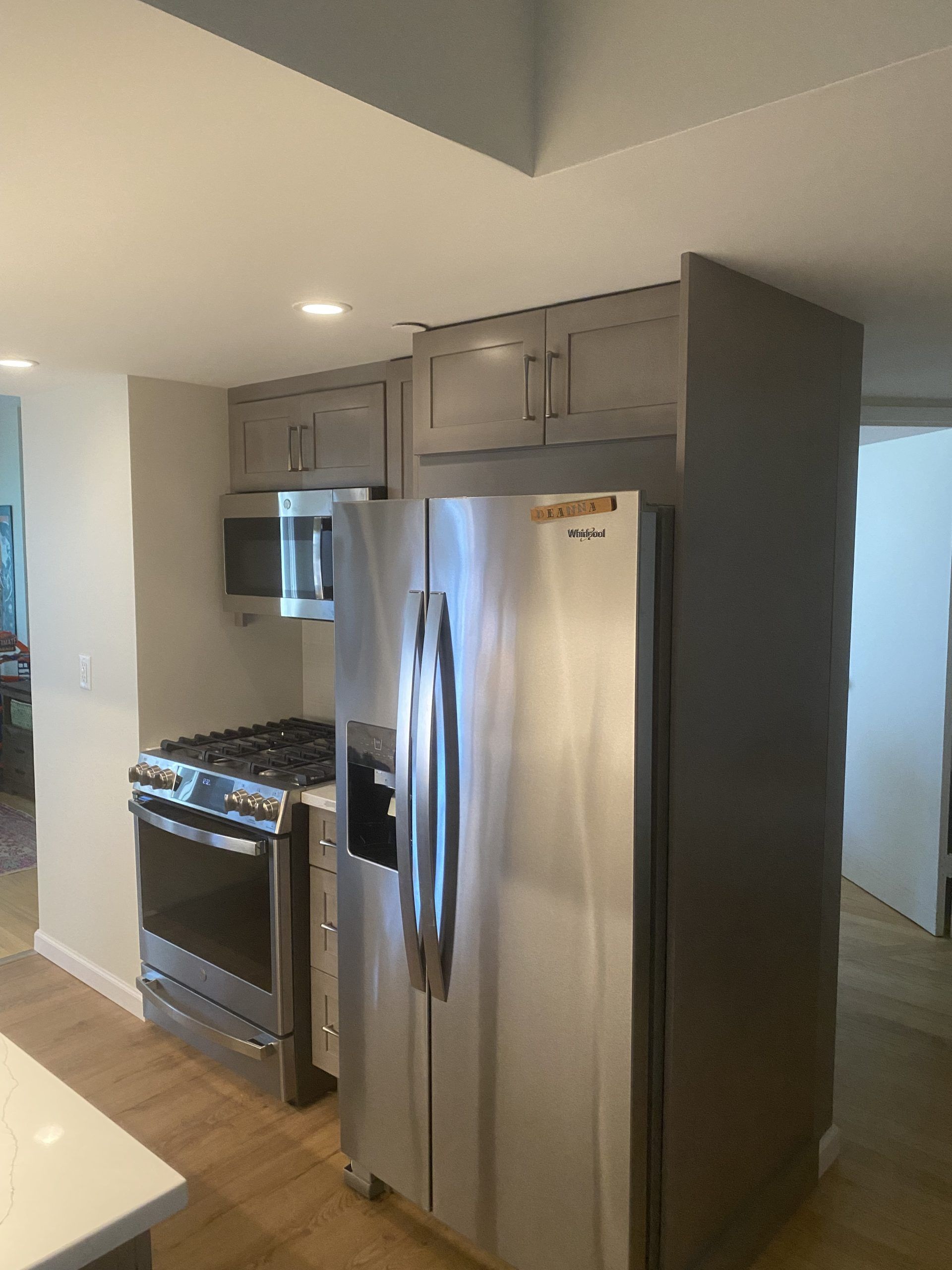 Stainless steel refrigerator and stove in a modern kitchen with gray cabinets and hardwood floor