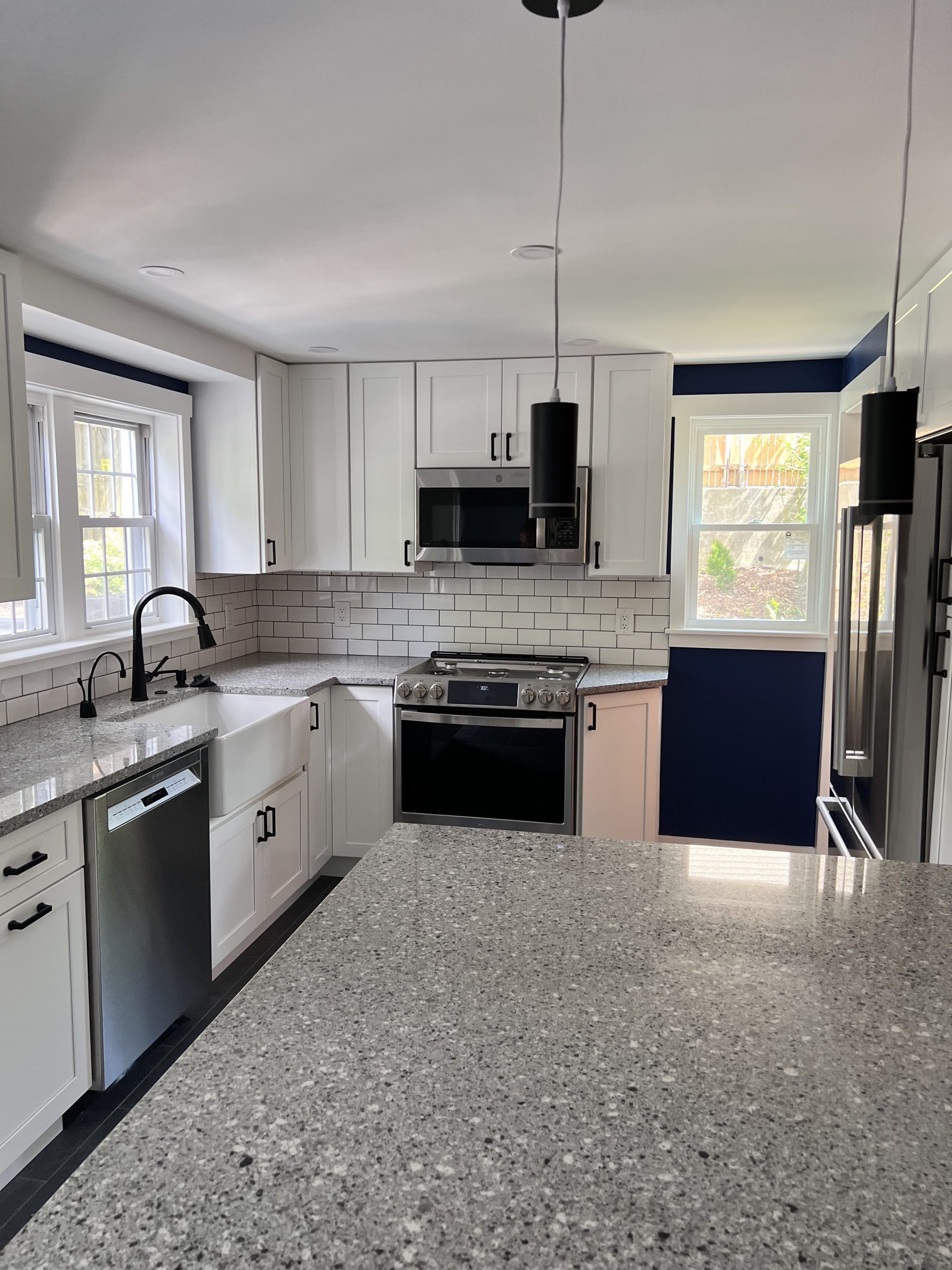 Modern kitchen with white cabinets, stainless appliances, blue accent wall, and speckled gray island countertop