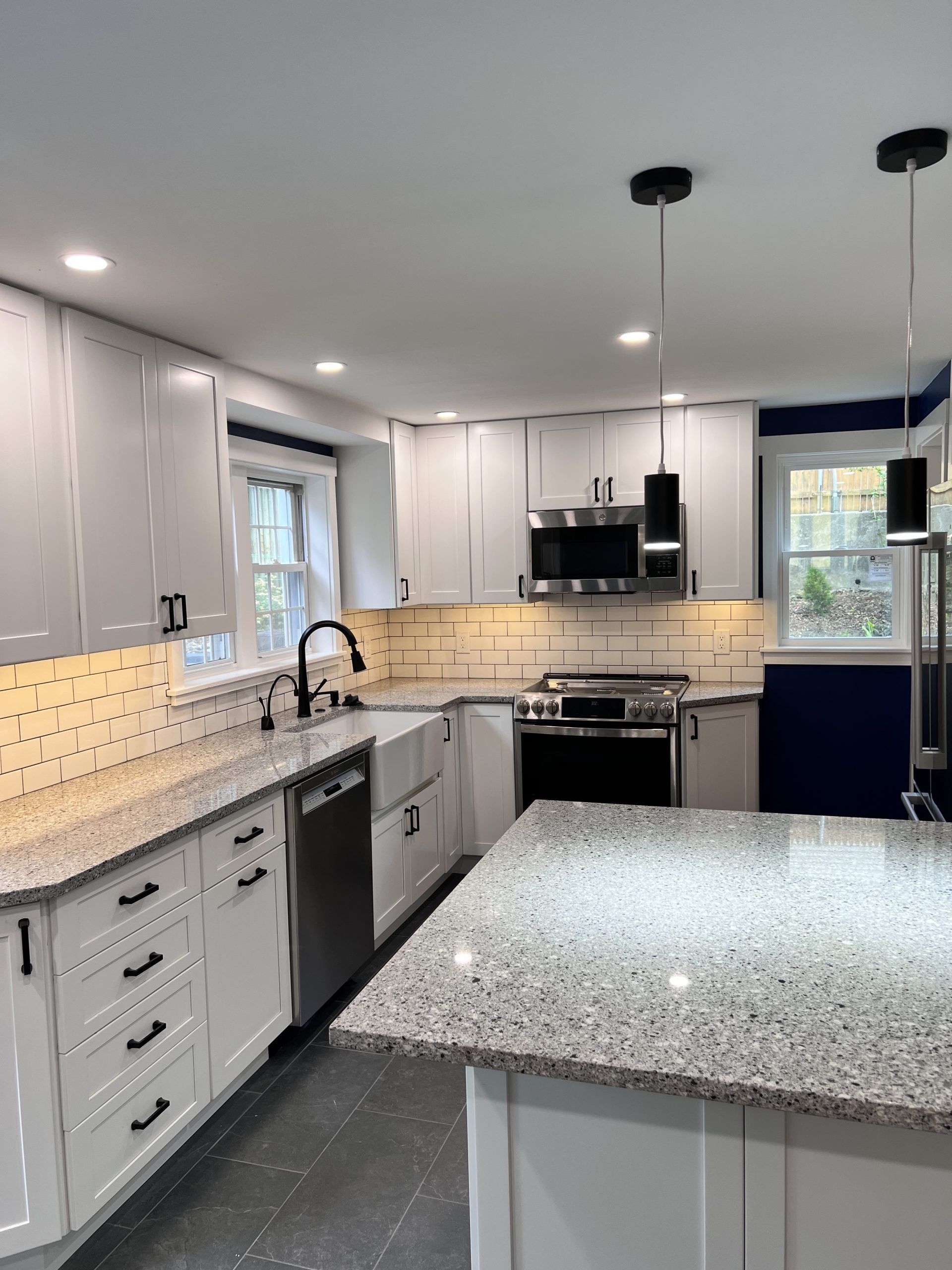 Modern kitchen with white cabinets, gray countertops, stainless appliances, and a large speckled island.