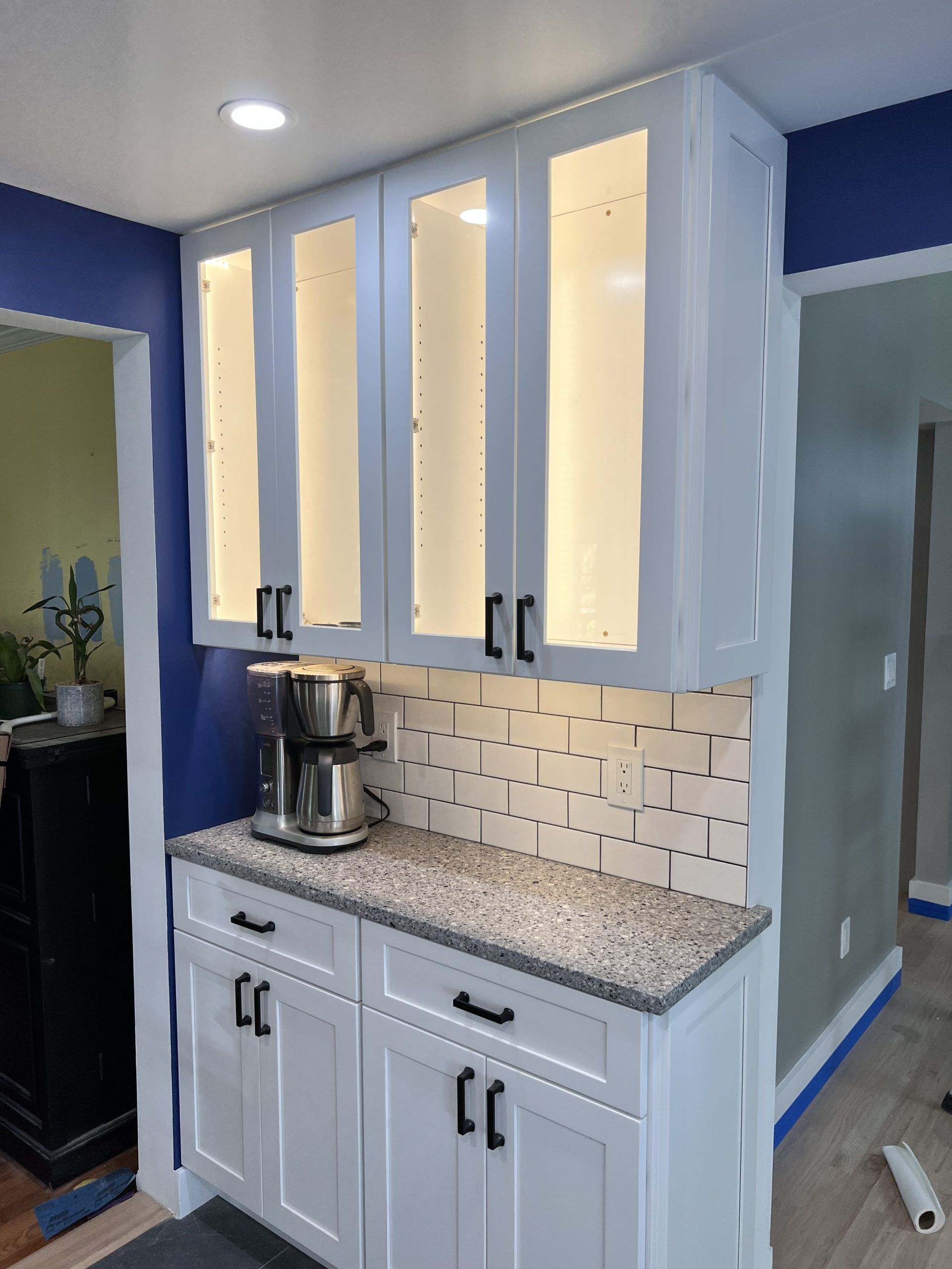White kitchen cabinets with under-cabinet lights, granite countertop, tile backsplash, and stand mixer against blue walls