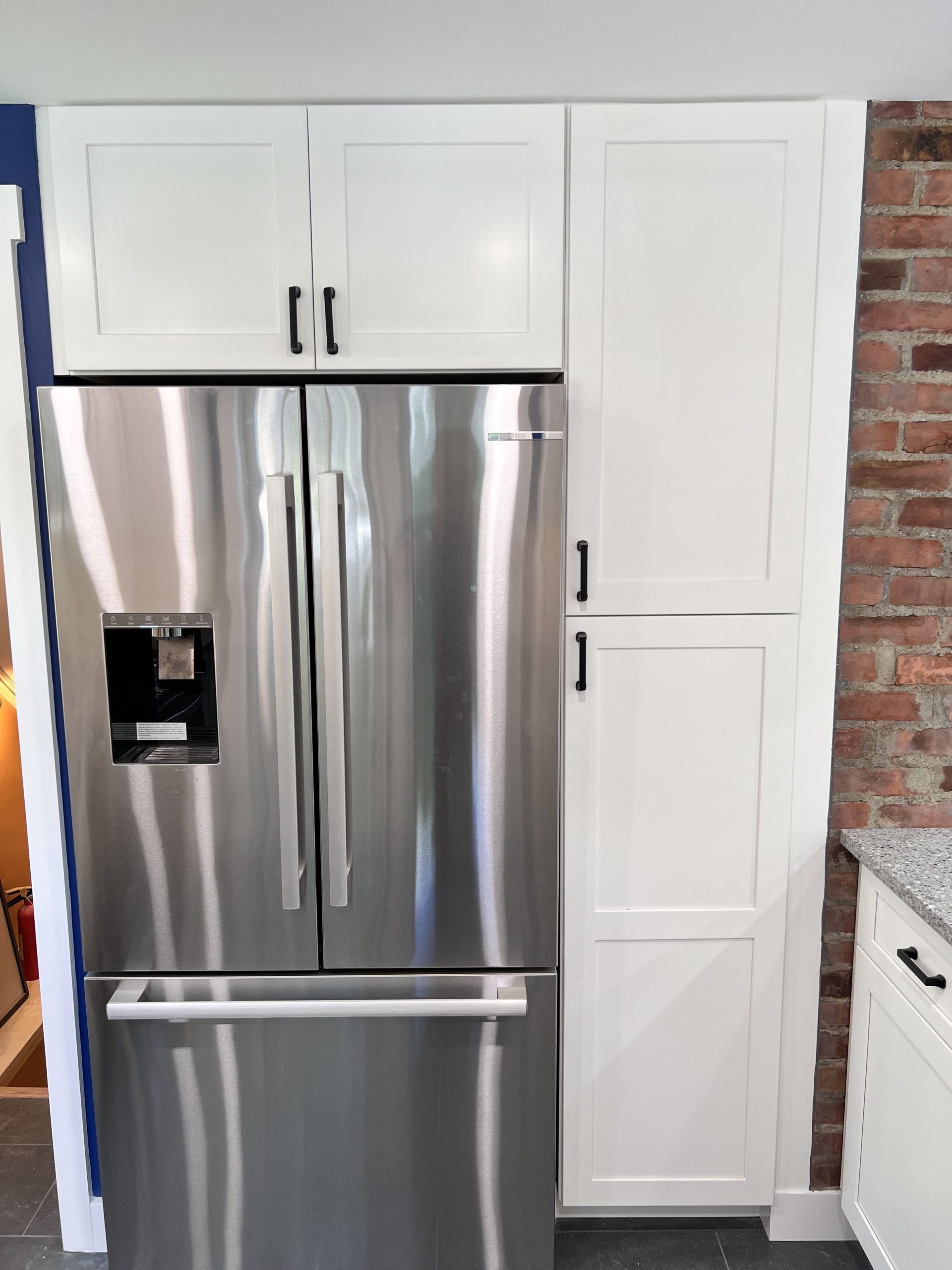 Stainless steel refrigerator with white cabinetry in a kitchen, beside a brick wall.