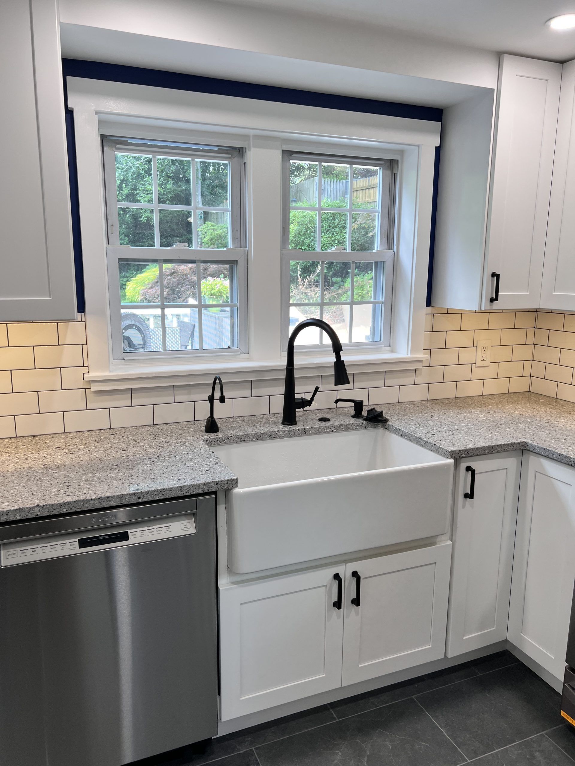 Modern kitchen with white cabinets, granite countertops, farmhouse sink, black faucet, and stainless dishwasher by window