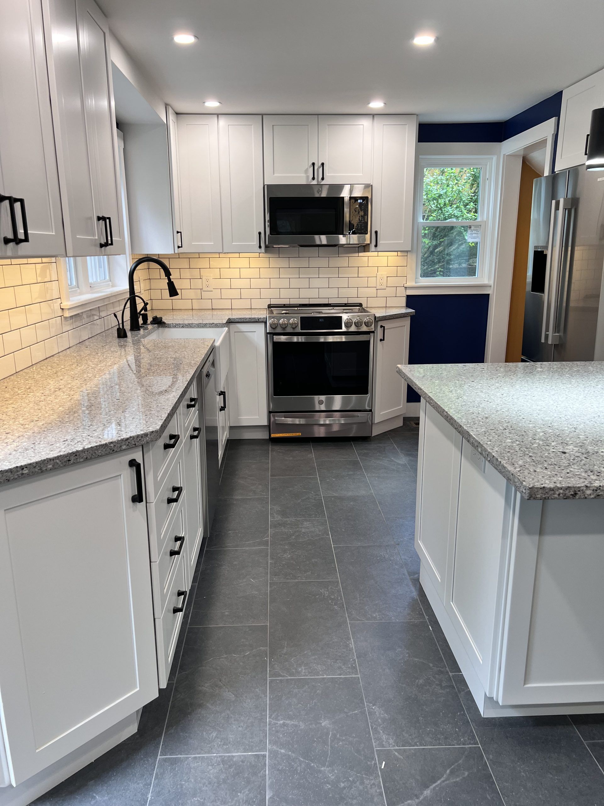 Bright white kitchen with granite countertops, stainless appliances, island, and dark tile floor.