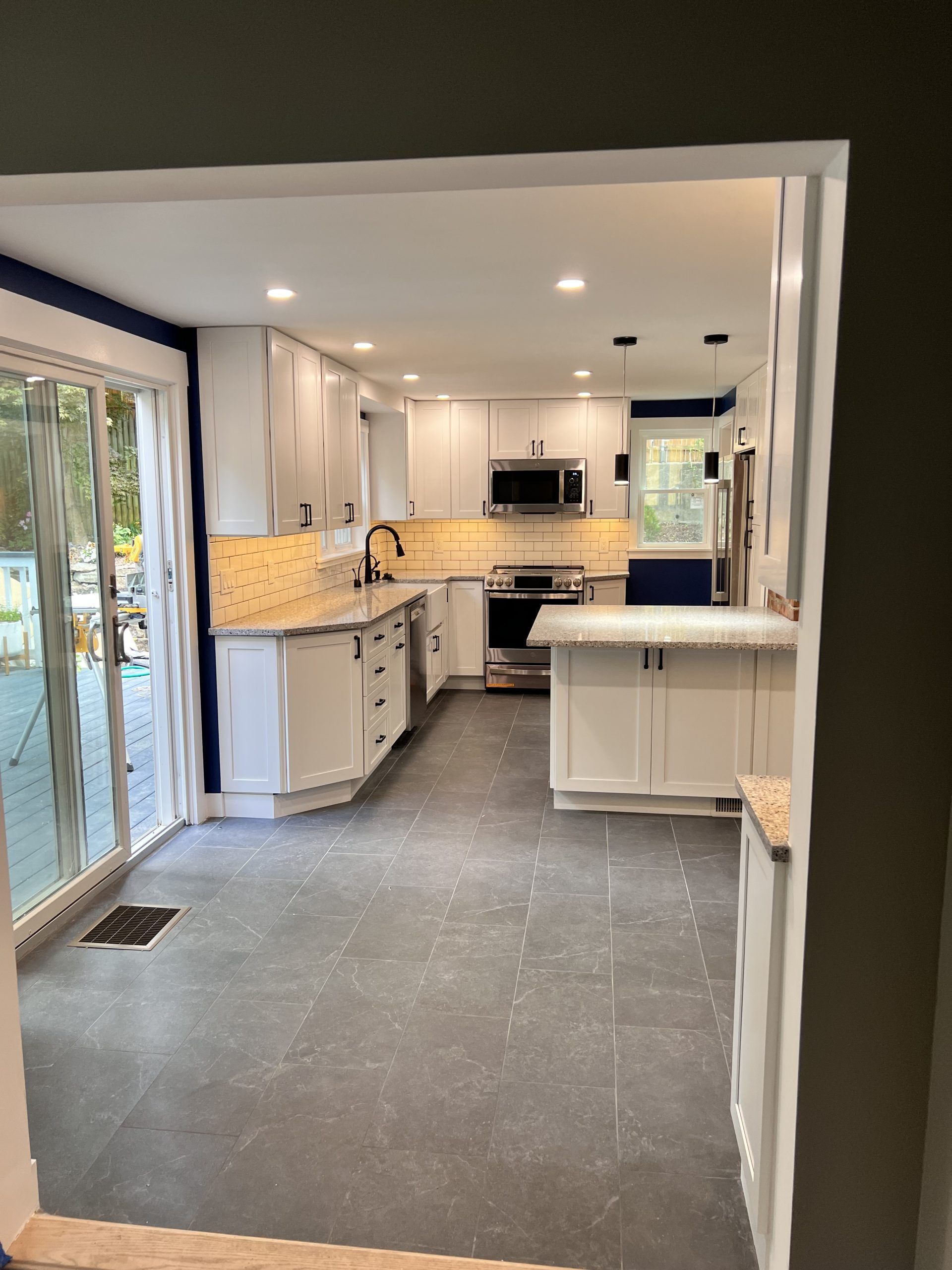 Bright modern kitchen with white cabinets, island, stainless appliances, and sliding glass doors to the left.