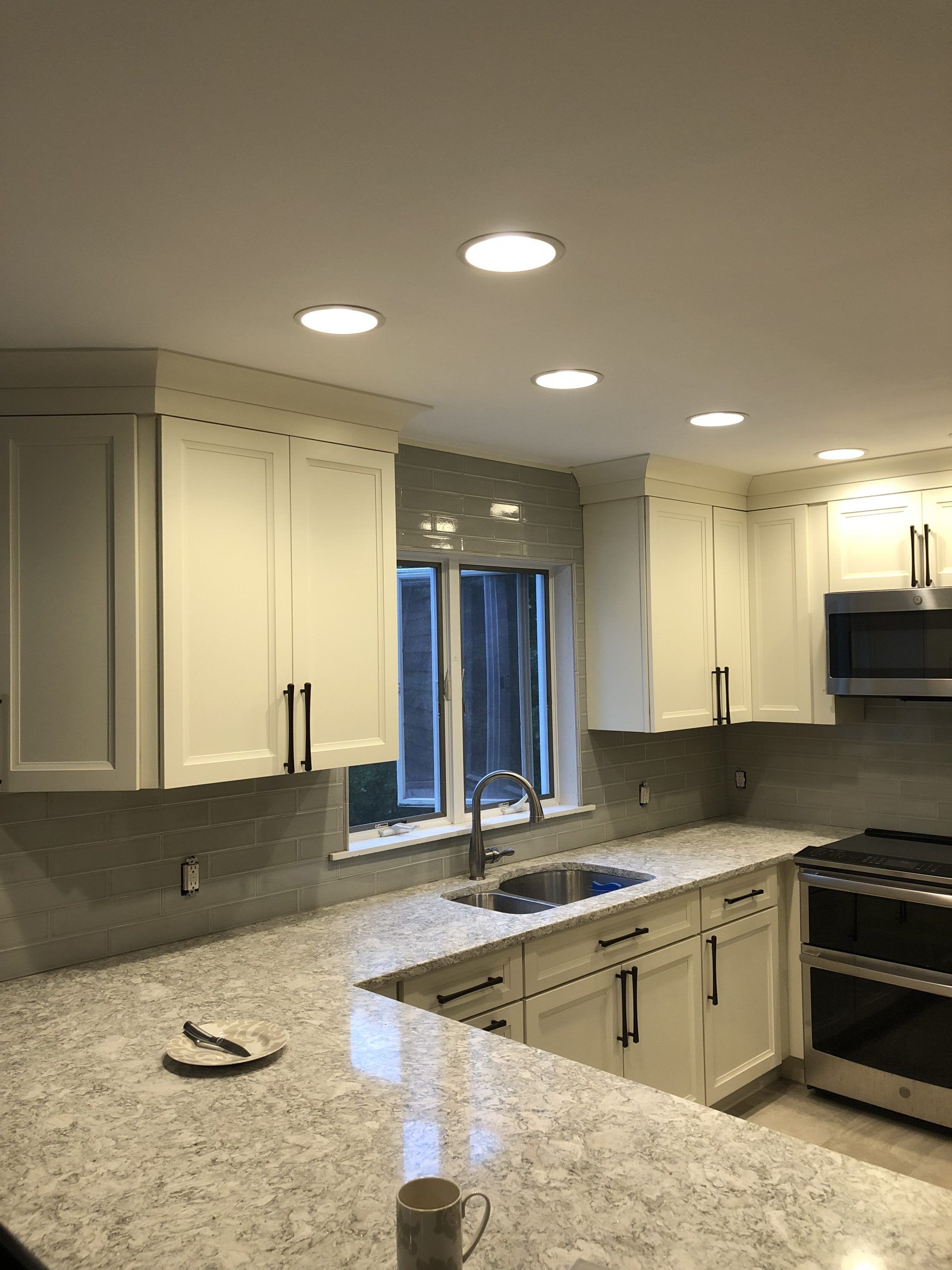 Modern kitchen with white cabinets, granite countertops, recessed lights, and a window above the sink.