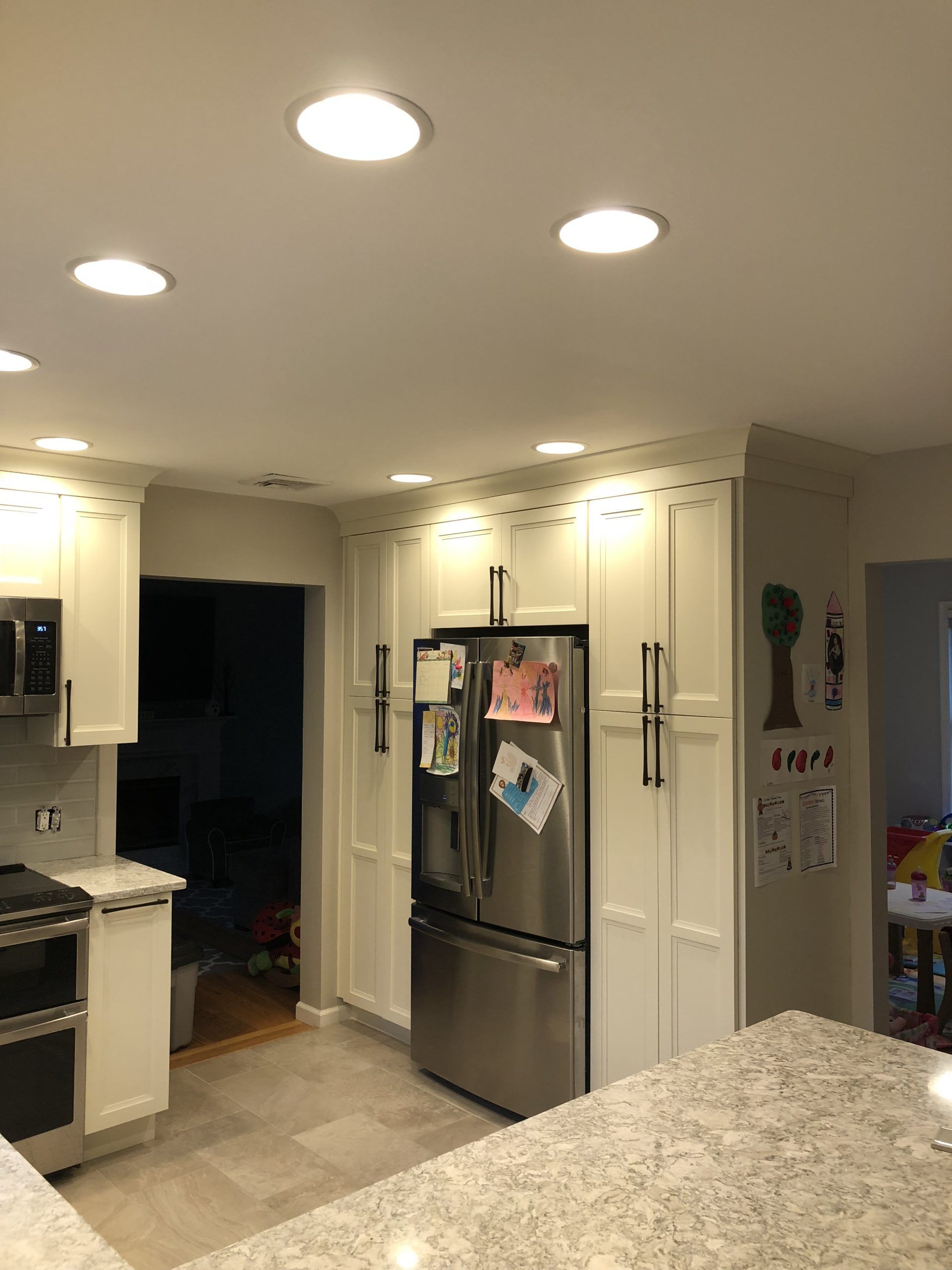 Bright kitchen with white cabinets, stainless steel fridge, and granite countertop under recessed lights