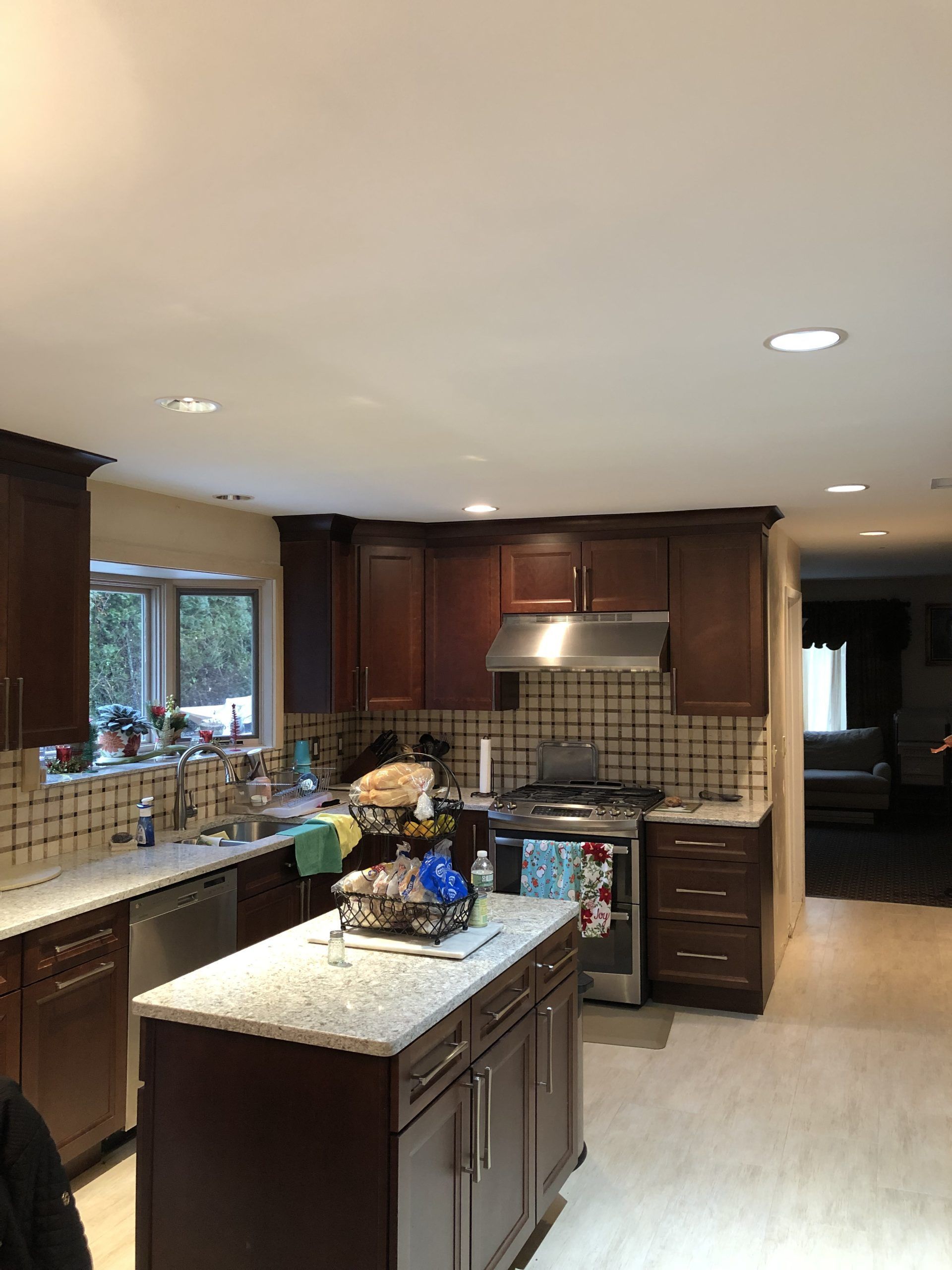 Modern kitchen with dark wood cabinets, granite island, stainless range hood, and a large window.