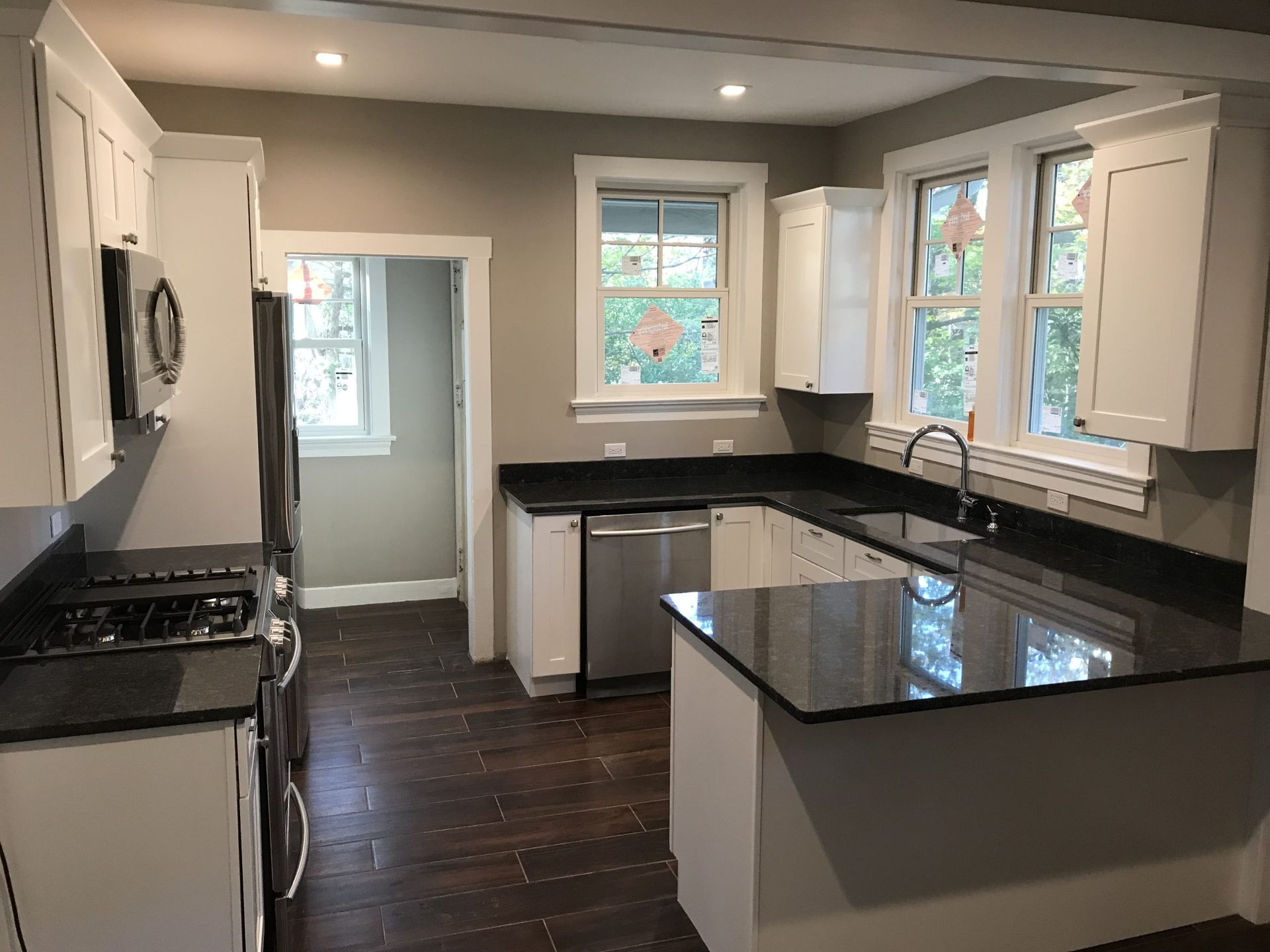 Modern kitchen with black countertops, white cabinets, dark wood floors, and two windows.