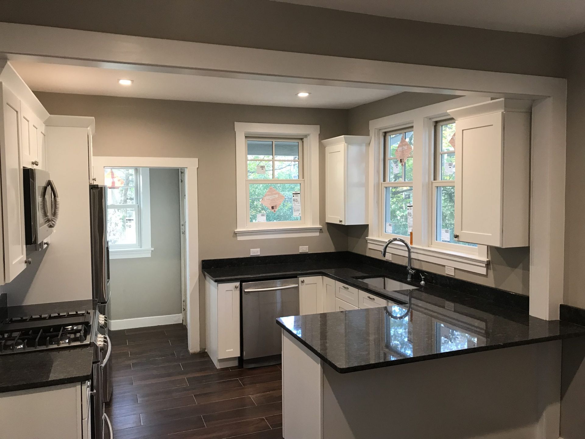 Modern kitchen with white cabinets, black countertops, stainless stove, and large windows.