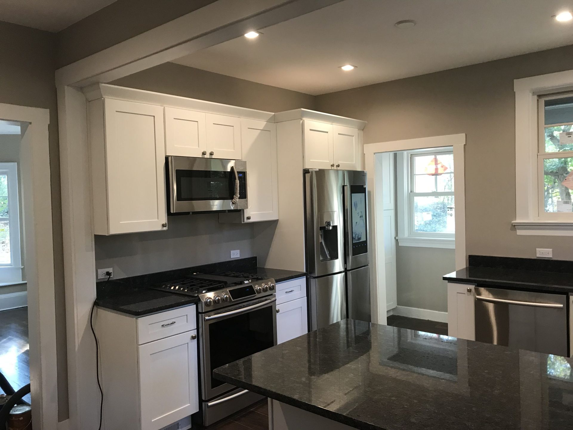 Modern kitchen with white cabinets, stainless appliances, black countertops, and a central island with granite top