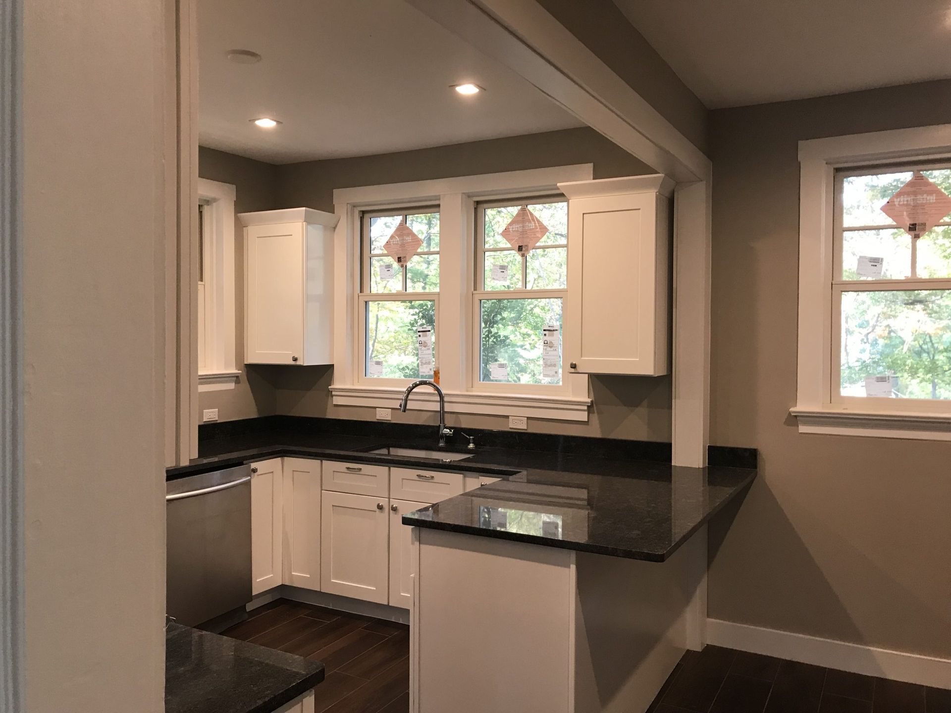 Small modern kitchen with white cabinets, black countertops, and two windows letting in daylight.