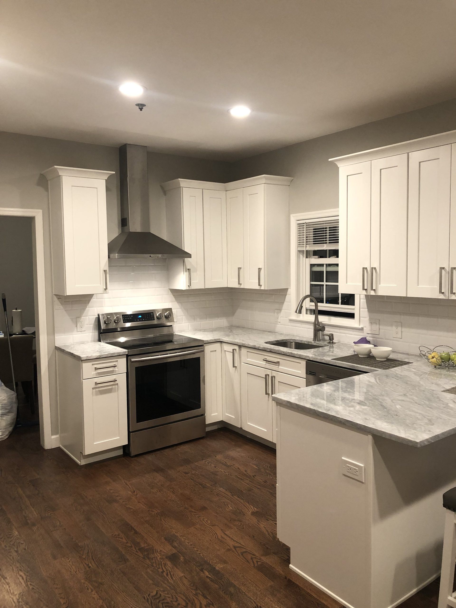 Modern white kitchen with stainless stove, gray countertops, and dark wood floors