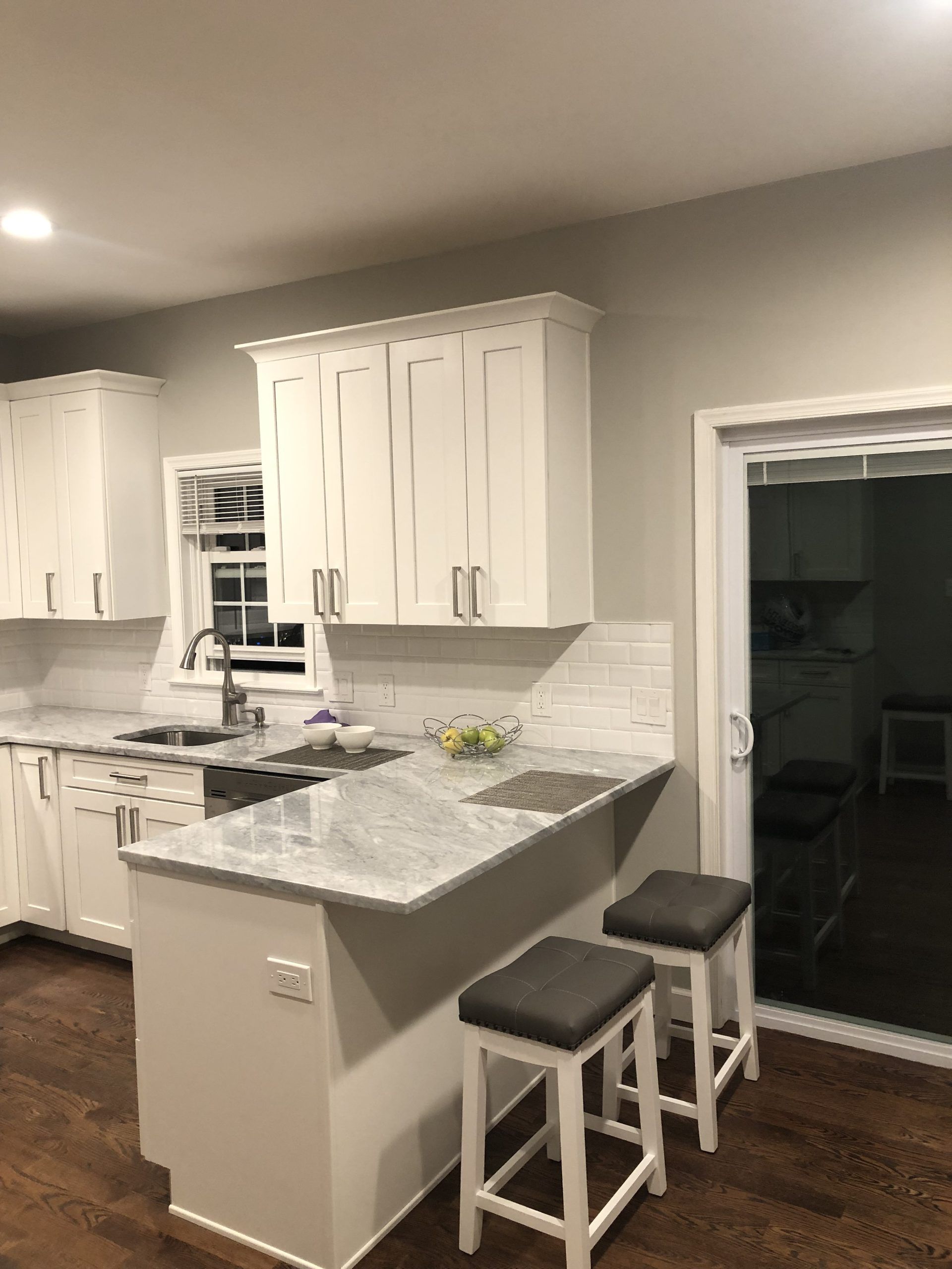 Modern kitchen with white cabinets, gray walls, granite island, and two bar stools by a sliding glass door