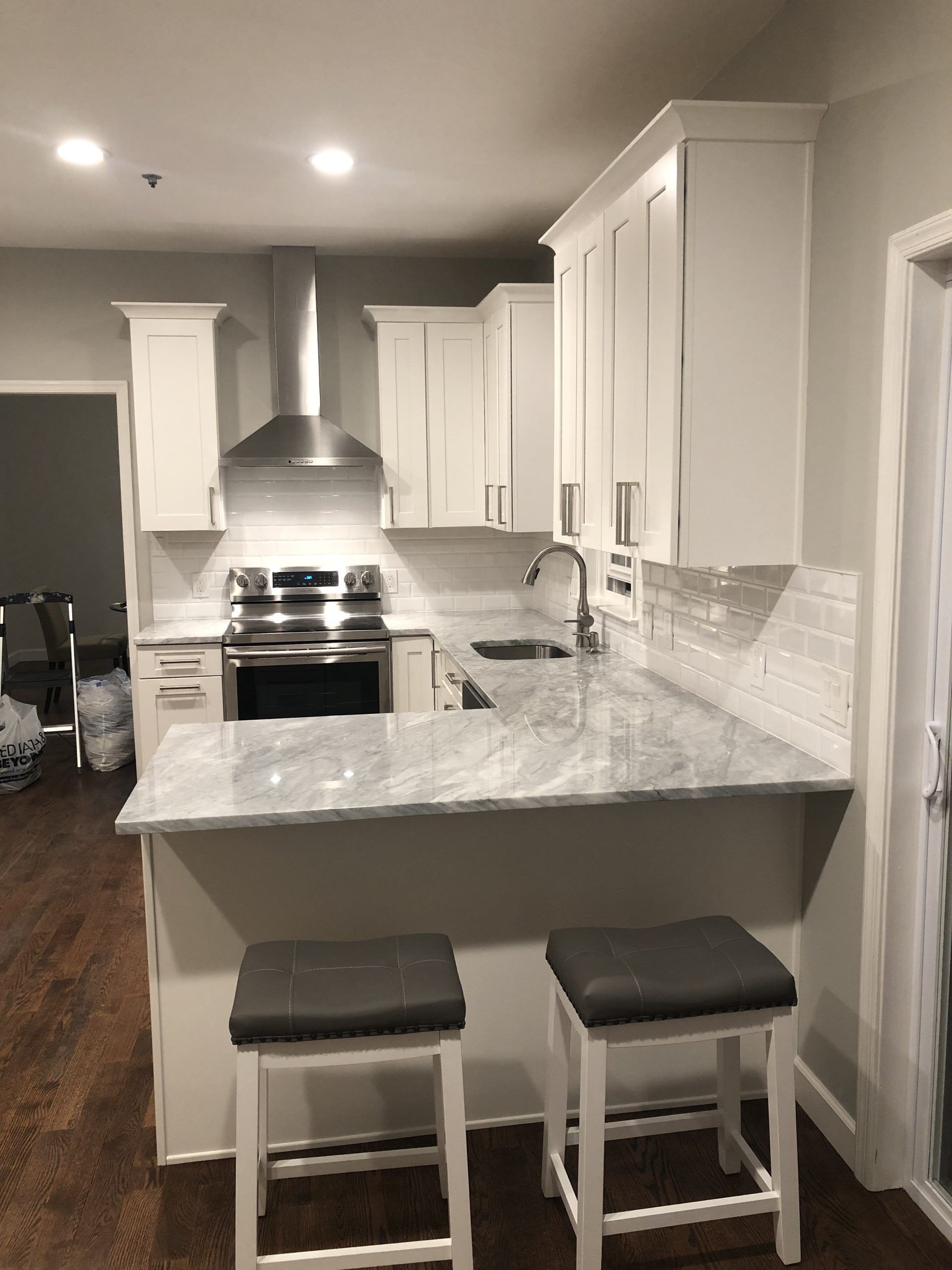 Bright white kitchen with marble island, two stools, stainless stove, and recessed ceiling lights