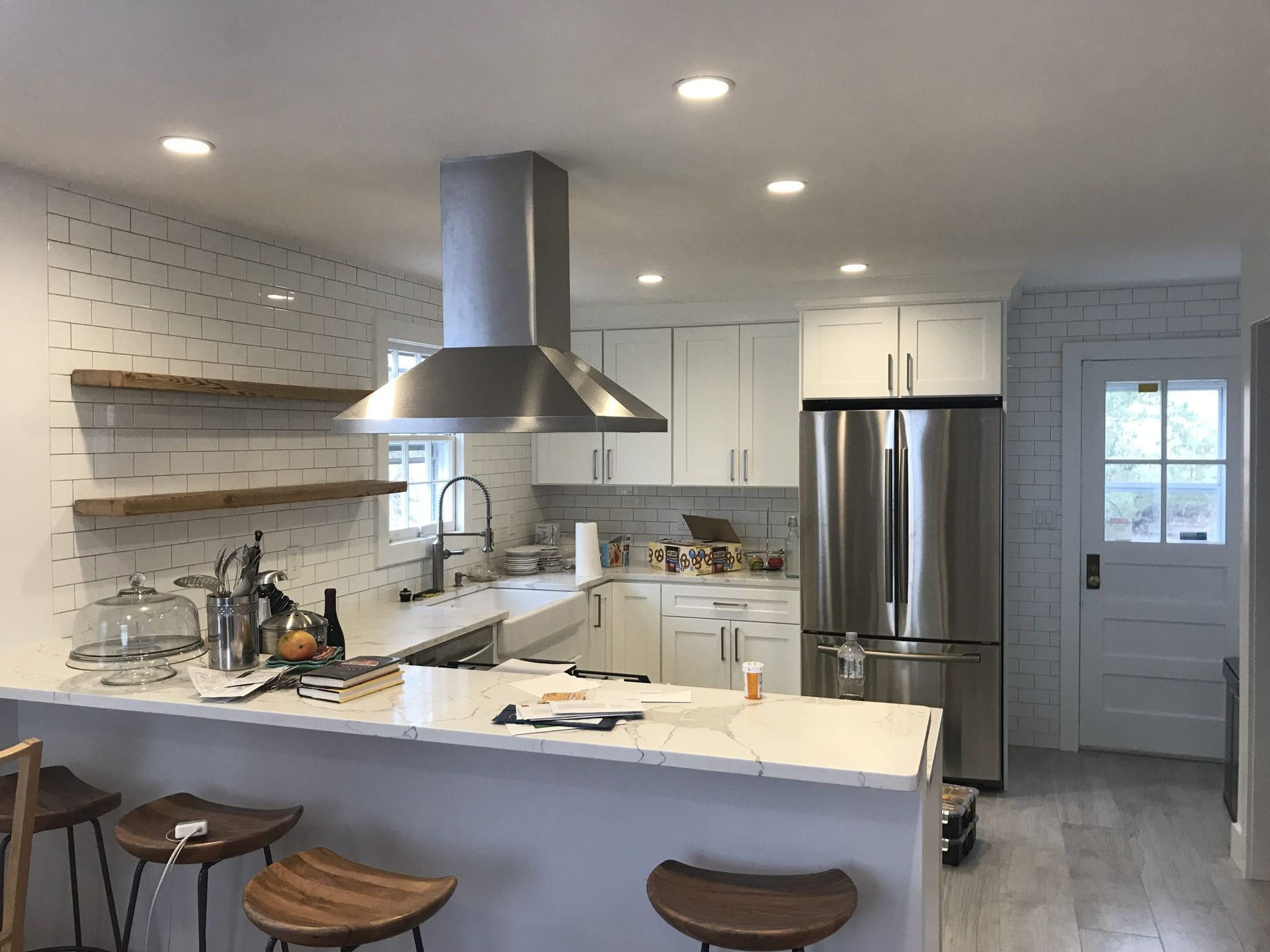 Modern white kitchen with island seating, stainless steel range hood, and stainless refrigerator