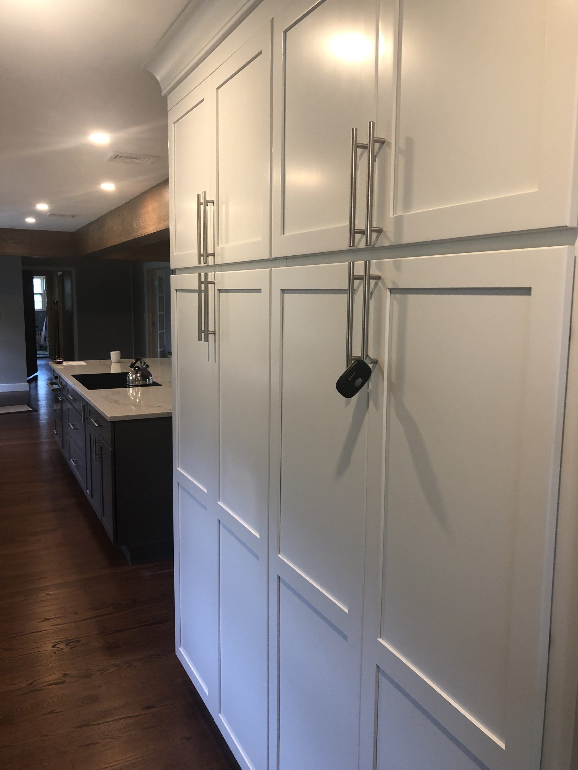 Narrow kitchen with white cabinets and stainless handles along a dark wood floor hallway.
