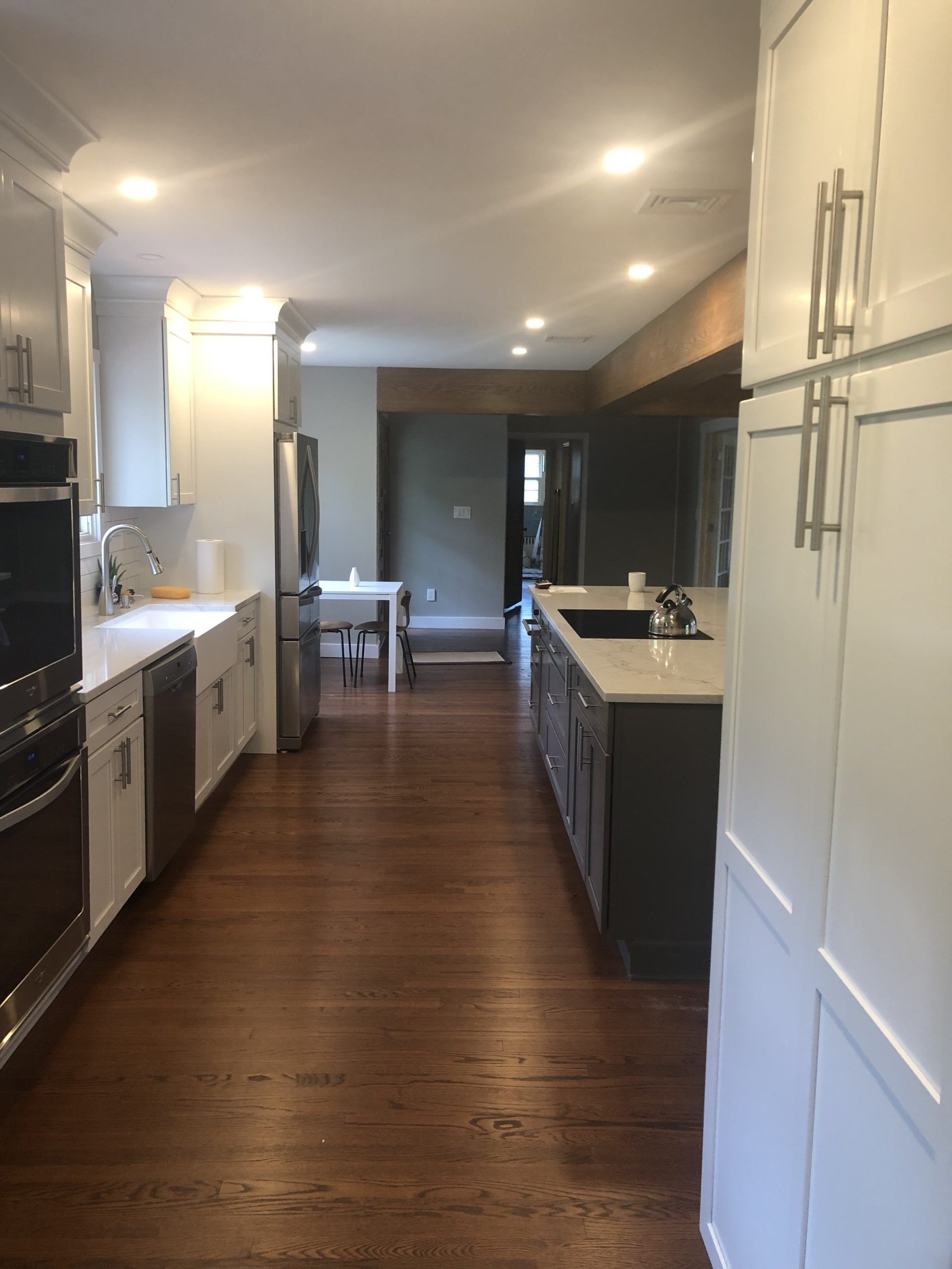 Bright modern kitchen with white cabinets, dark wood floor, and a dining area in the back.