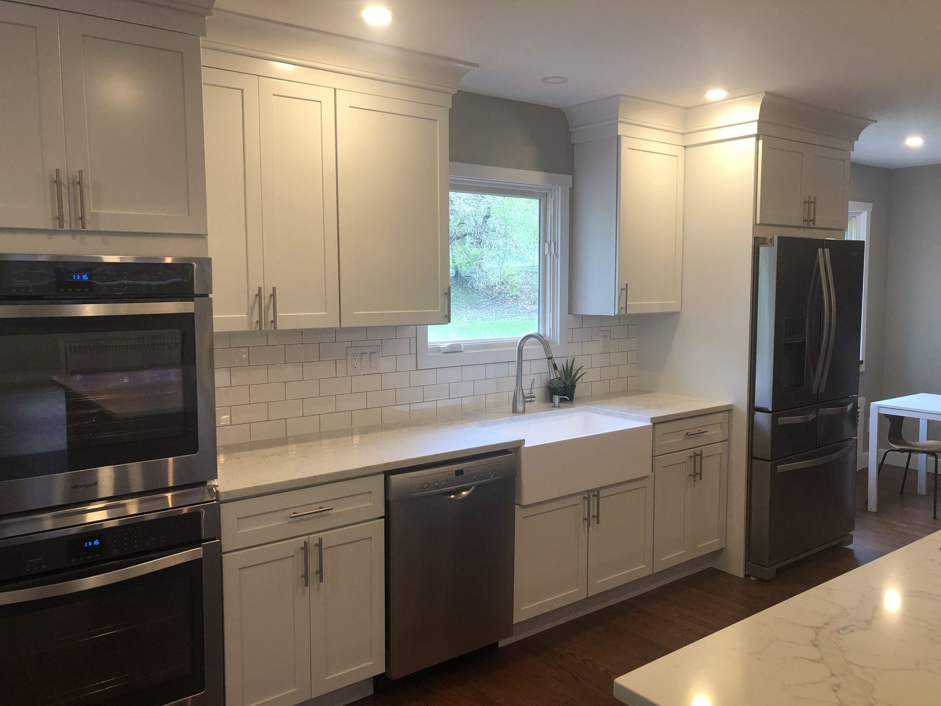 Modern white kitchen with island, built-in oven, dishwasher, black refrigerator, and large window.