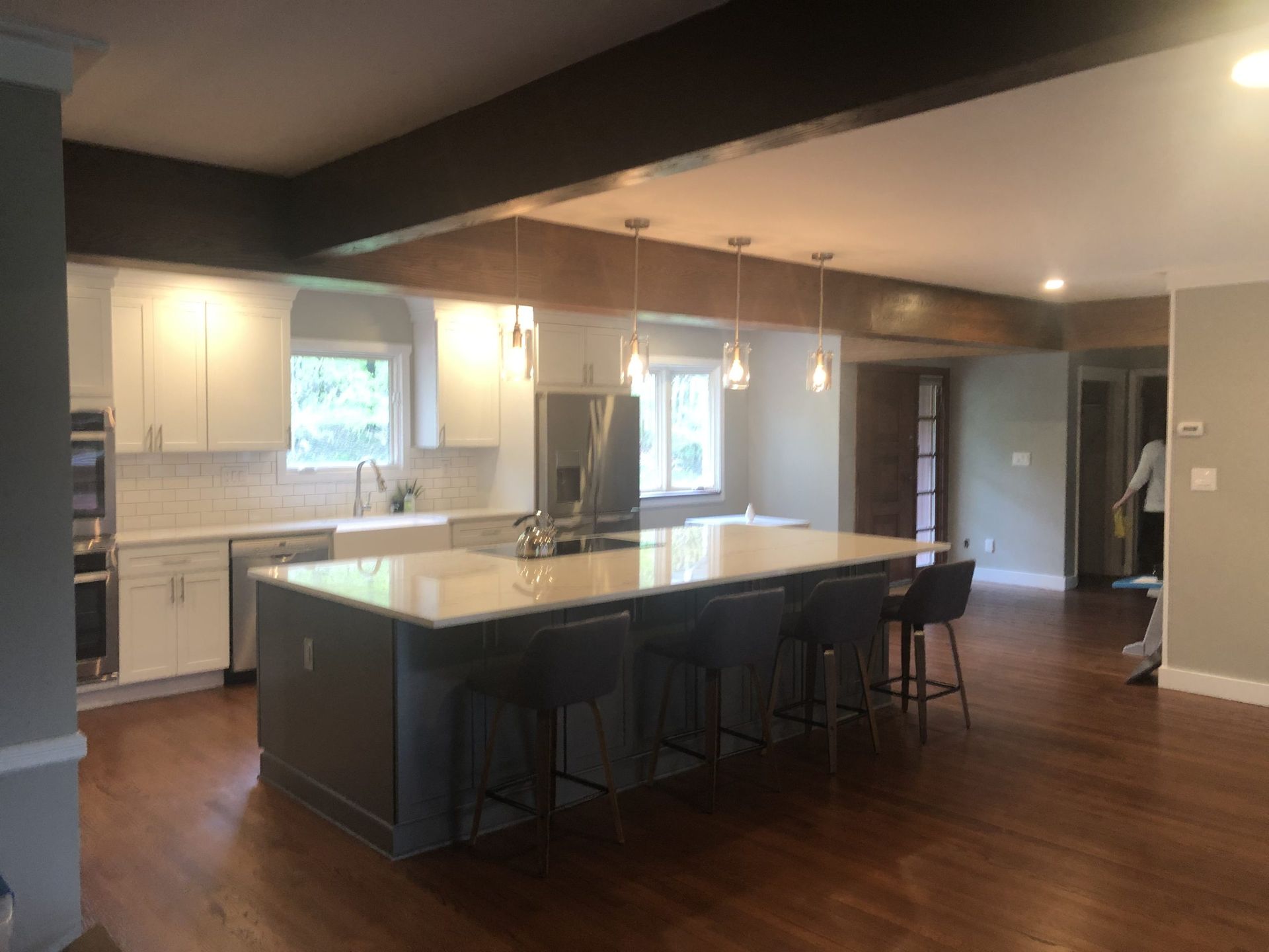 Modern kitchen with a large island, dark stools, white cabinets, and hardwood floors