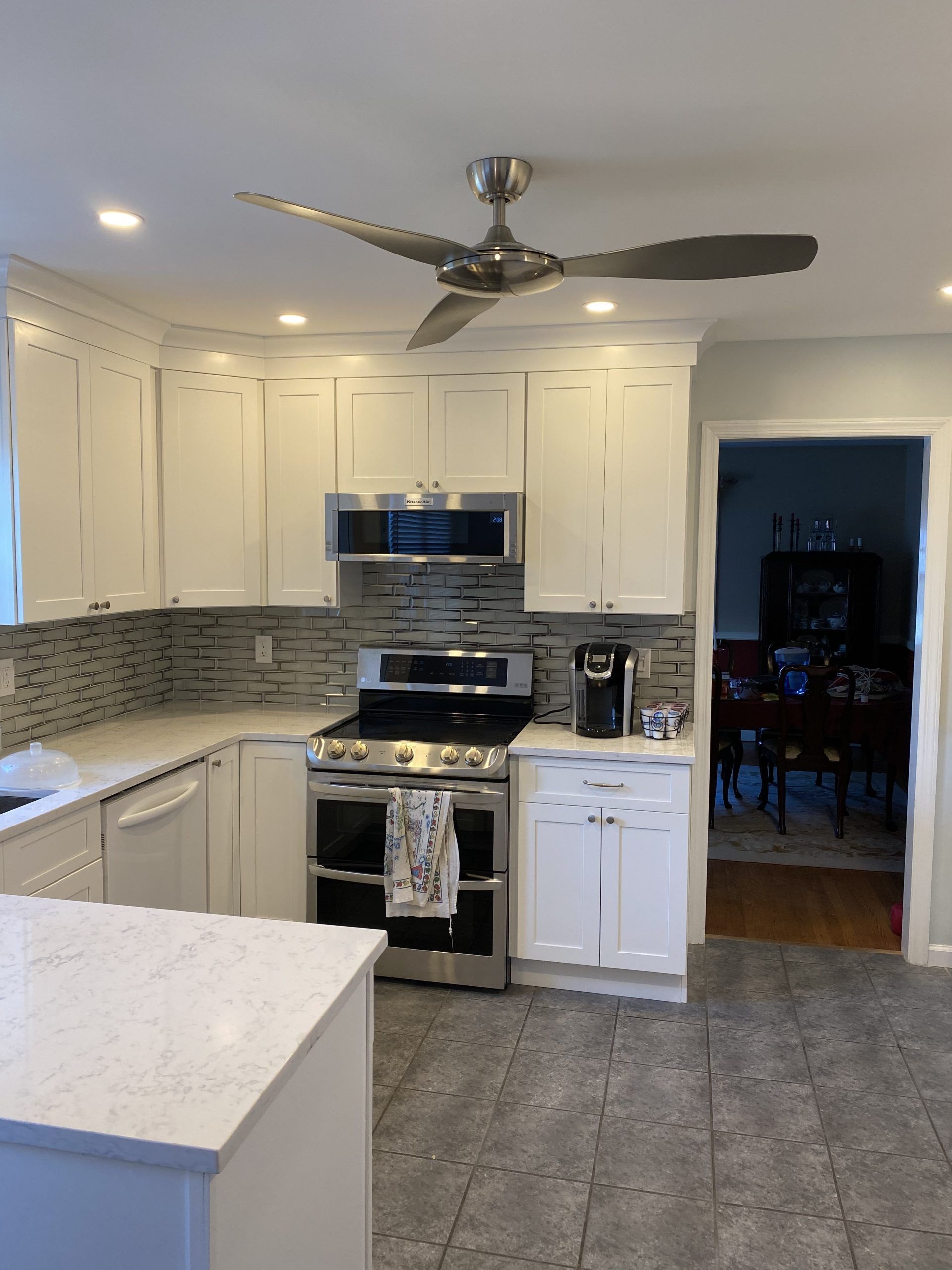 Bright white kitchen with stainless steel appliances, tile backsplash, and ceiling fan.