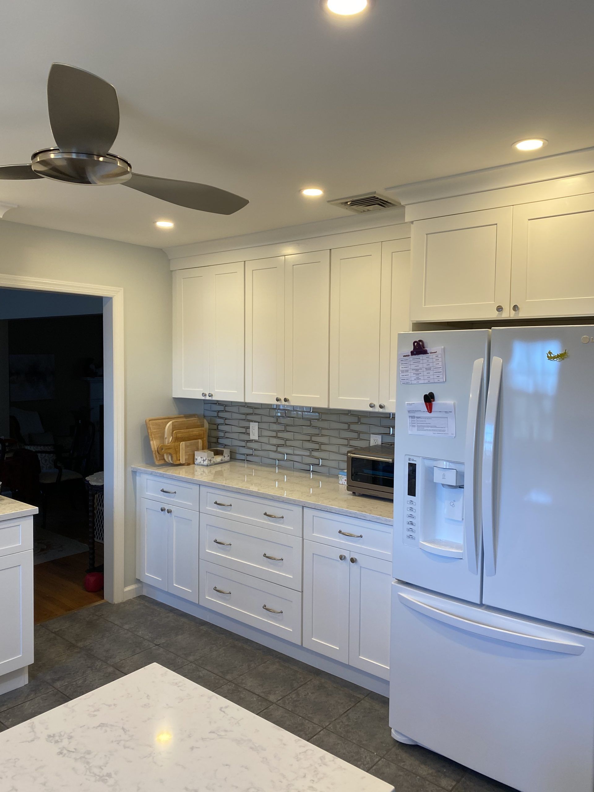 Bright kitchen with white cabinets, stainless fridge, mosaic backsplash, ceiling fan, and granite island countertop
