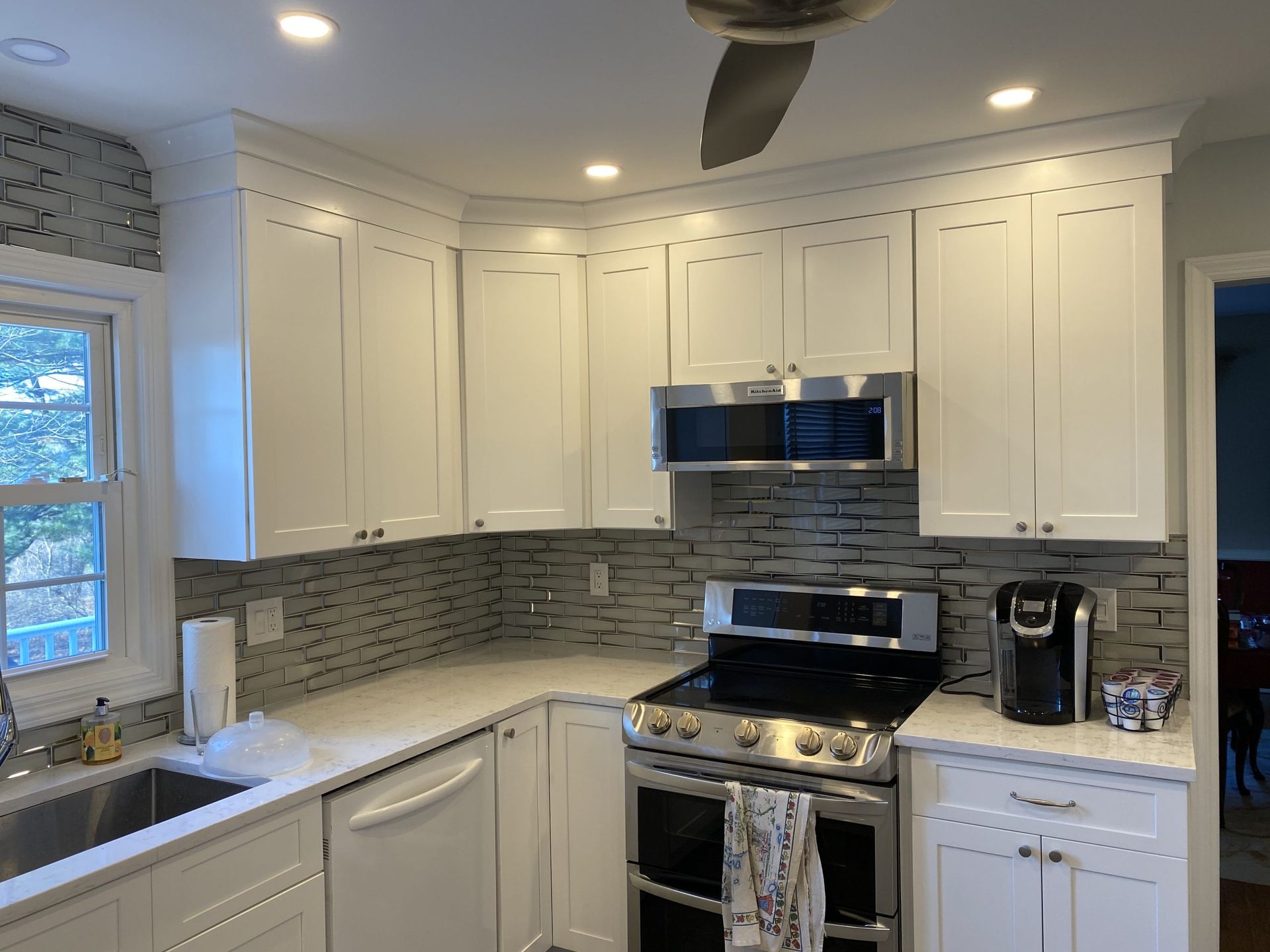 Modern white kitchen with stainless steel stove, microwave, gray backsplash, and recessed ceiling lights