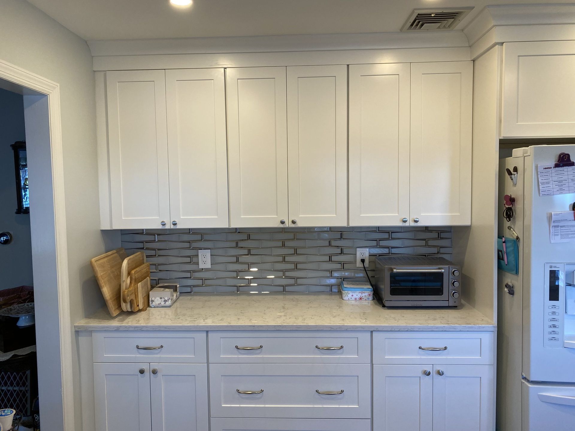 White kitchen with cabinets, gray tile backsplash, microwave, and refrigerator beside a doorway