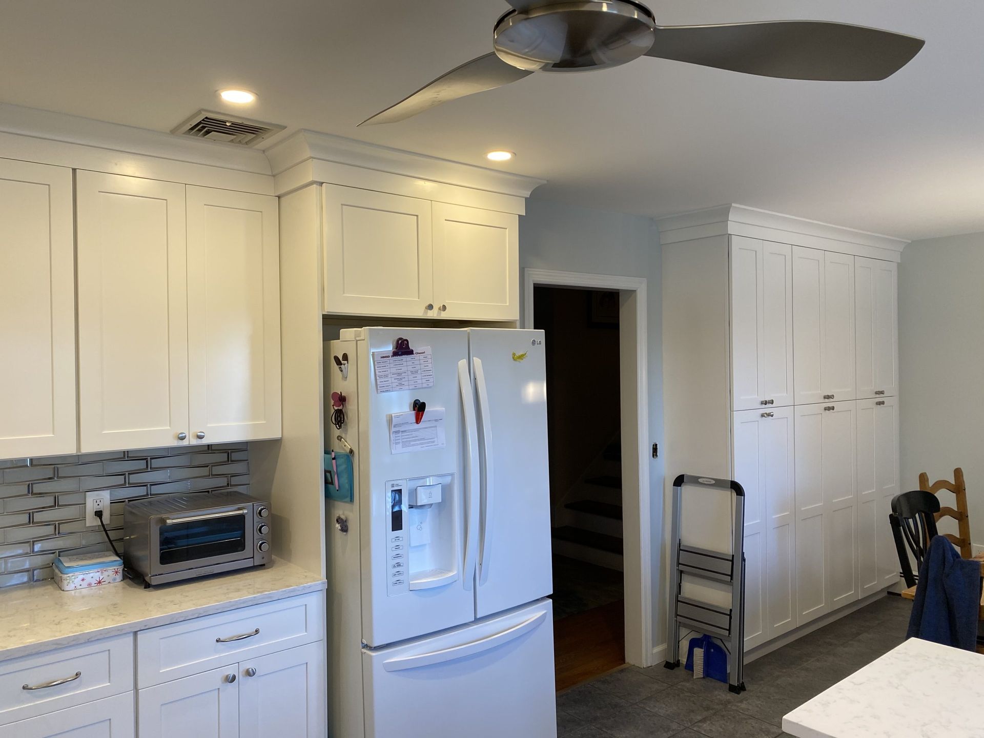 Bright white kitchen with island, ceiling fan, refrigerator, and tiled backsplash.