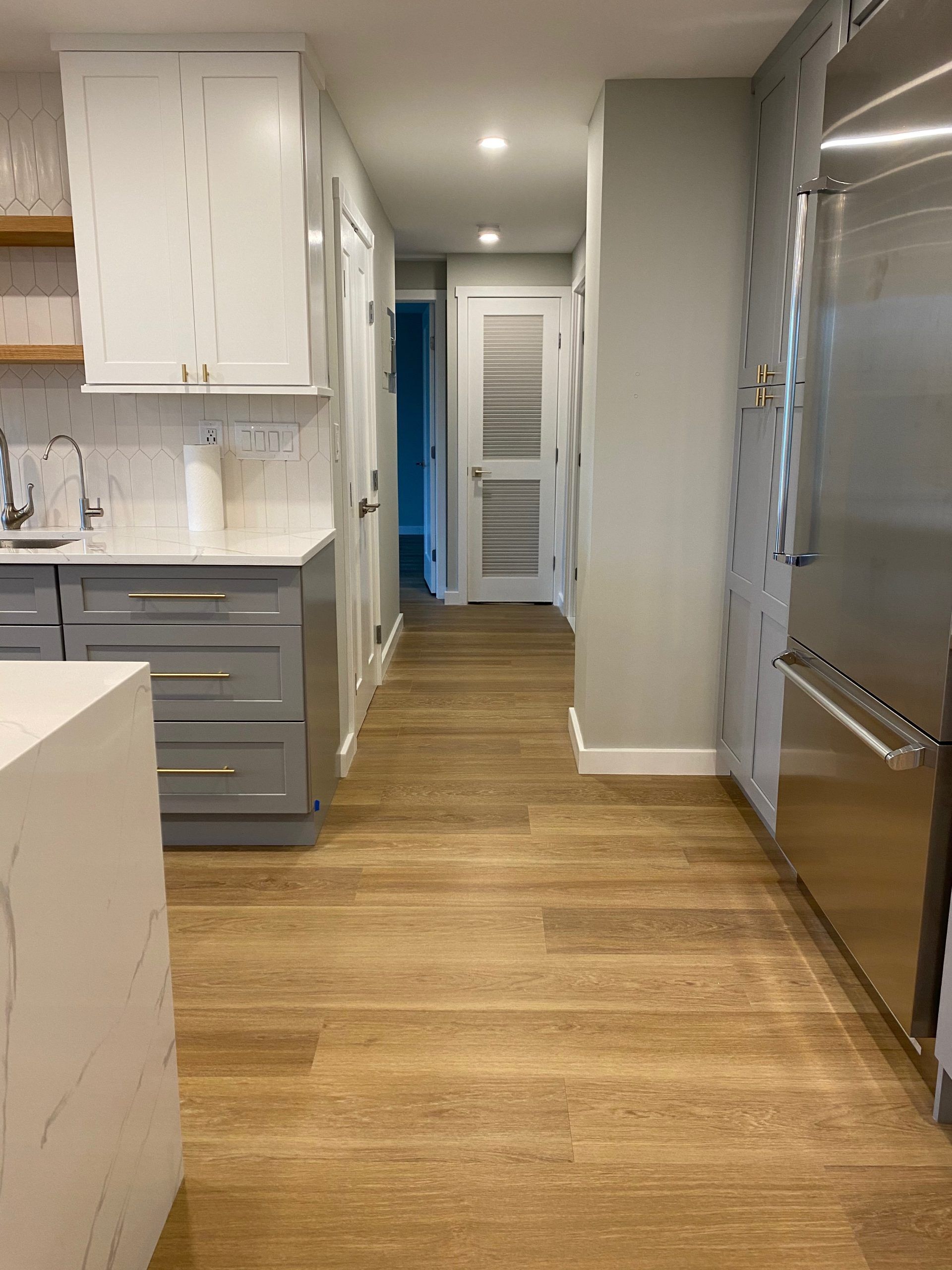 Bright kitchen hallway with white cabinets, wood floors, and stainless steel appliances