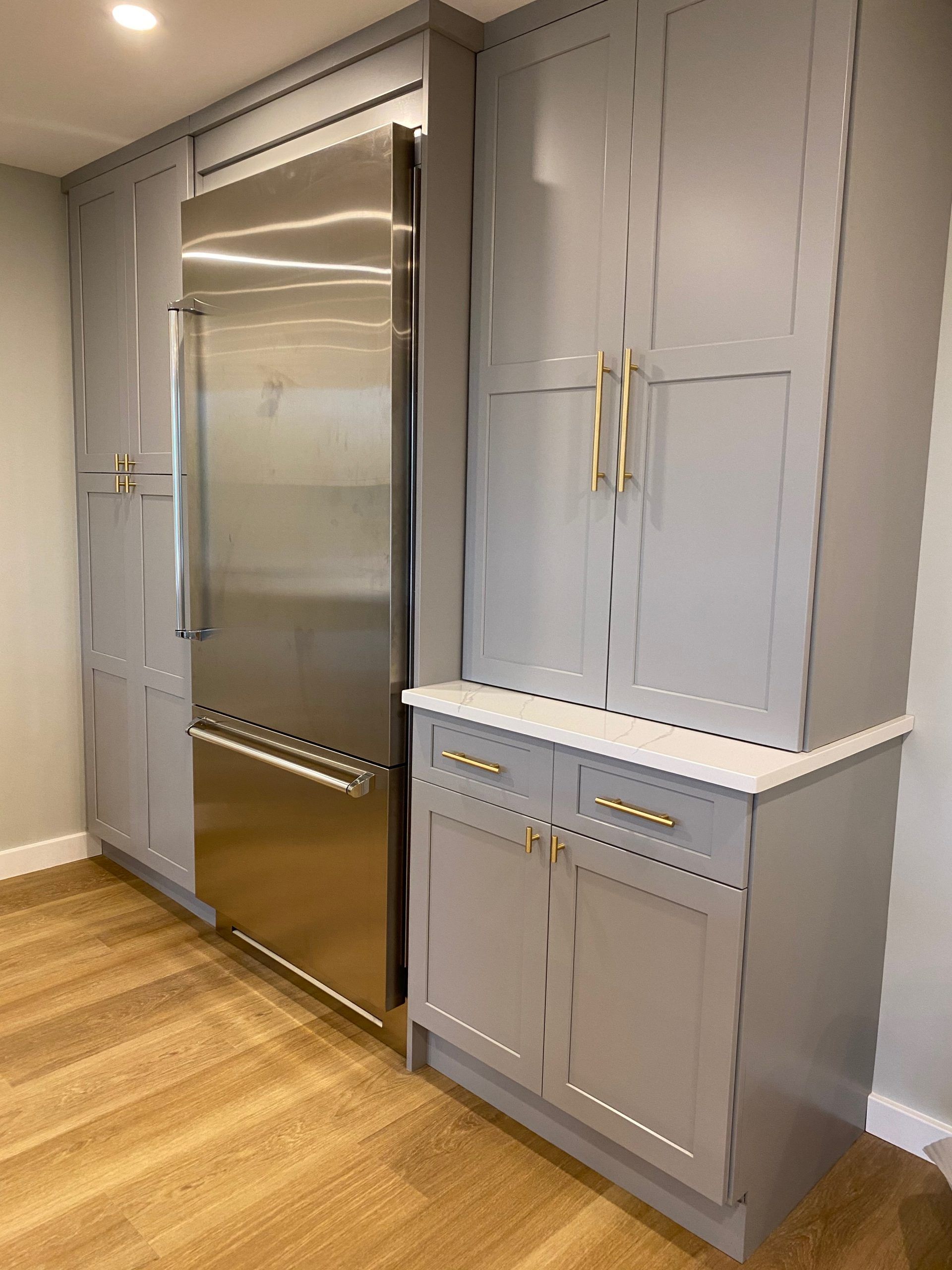 Built-in gray cabinetry with a stainless-steel refrigerator and wood floor in a modern kitchen.