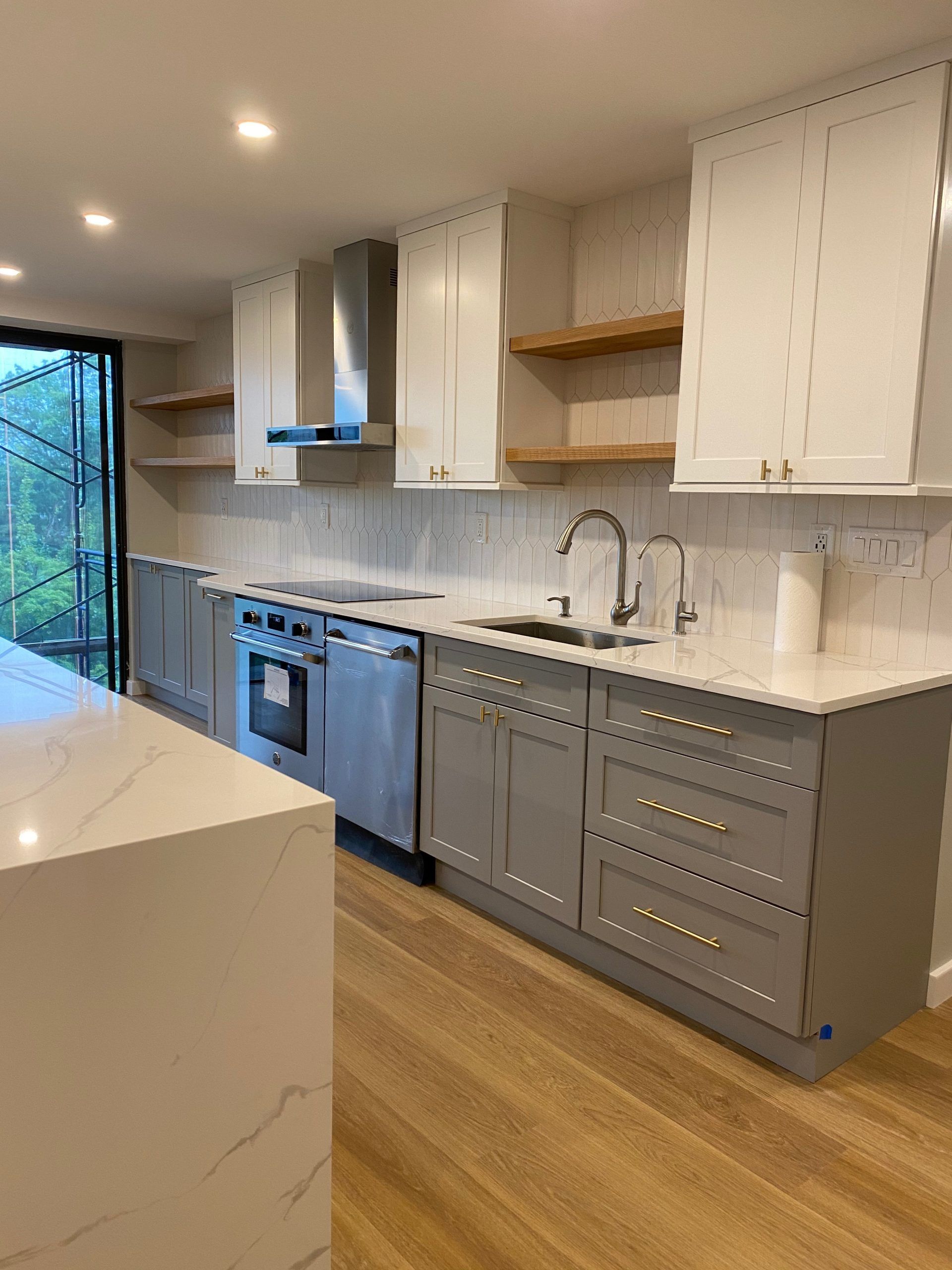 Modern kitchen with gray cabinets, white countertops, stainless appliances, and wooden floorboards.