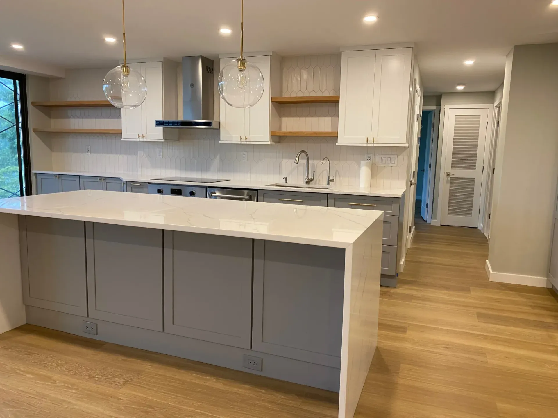 Modern kitchen with white island, gray cabinets, pendant lights, and wood flooring