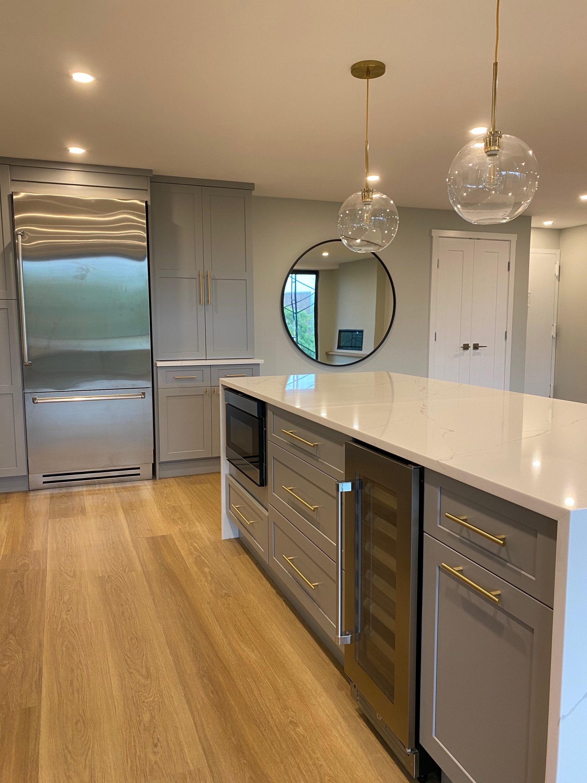 Modern kitchen with stainless steel appliances, white island, pendant lights, and wood floors.