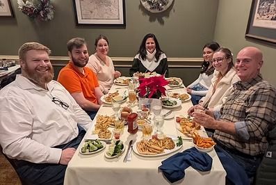 Group of people seated around a table in a restaurant; eating, conversing, and smiling.