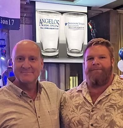 Two men pose for a photo with two branded pint glasses in the background.